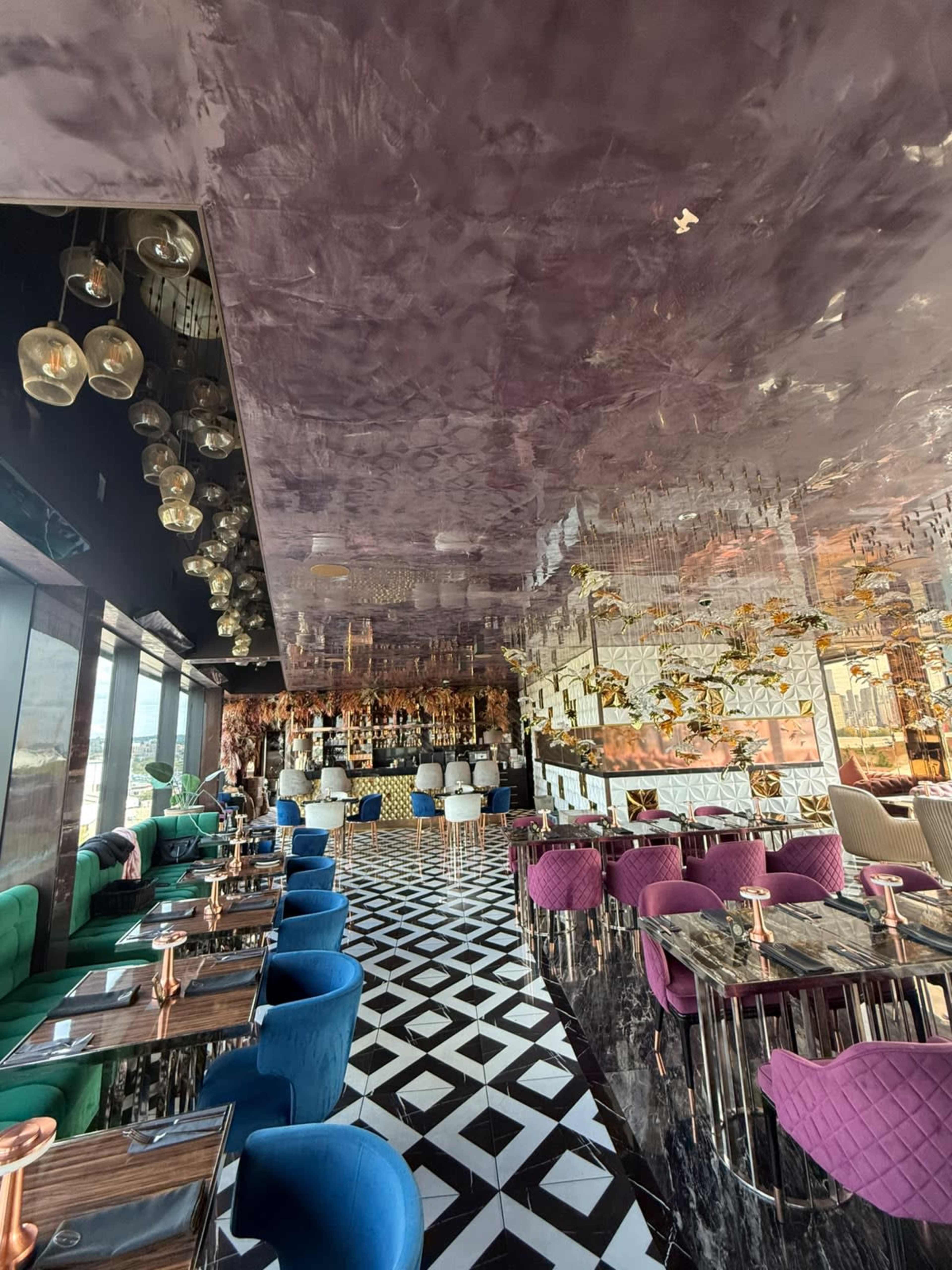 The image shows a modern restaurant interior with a glossy purple ceiling, patterned black and white floors, and colorful seating arranged around tables.