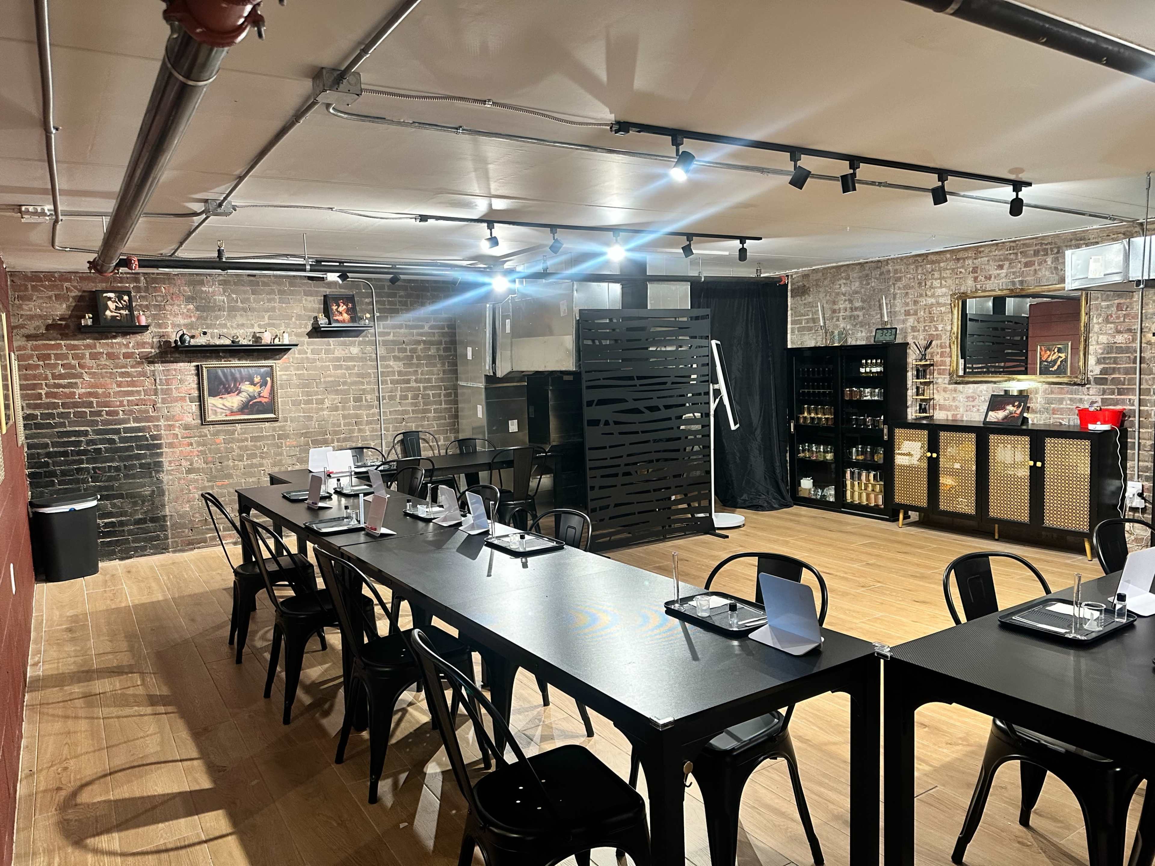 The image shows a spacious dining area with a long black table set for a meal, surrounded by black chairs, exposed brick walls, and warm wooden flooring.