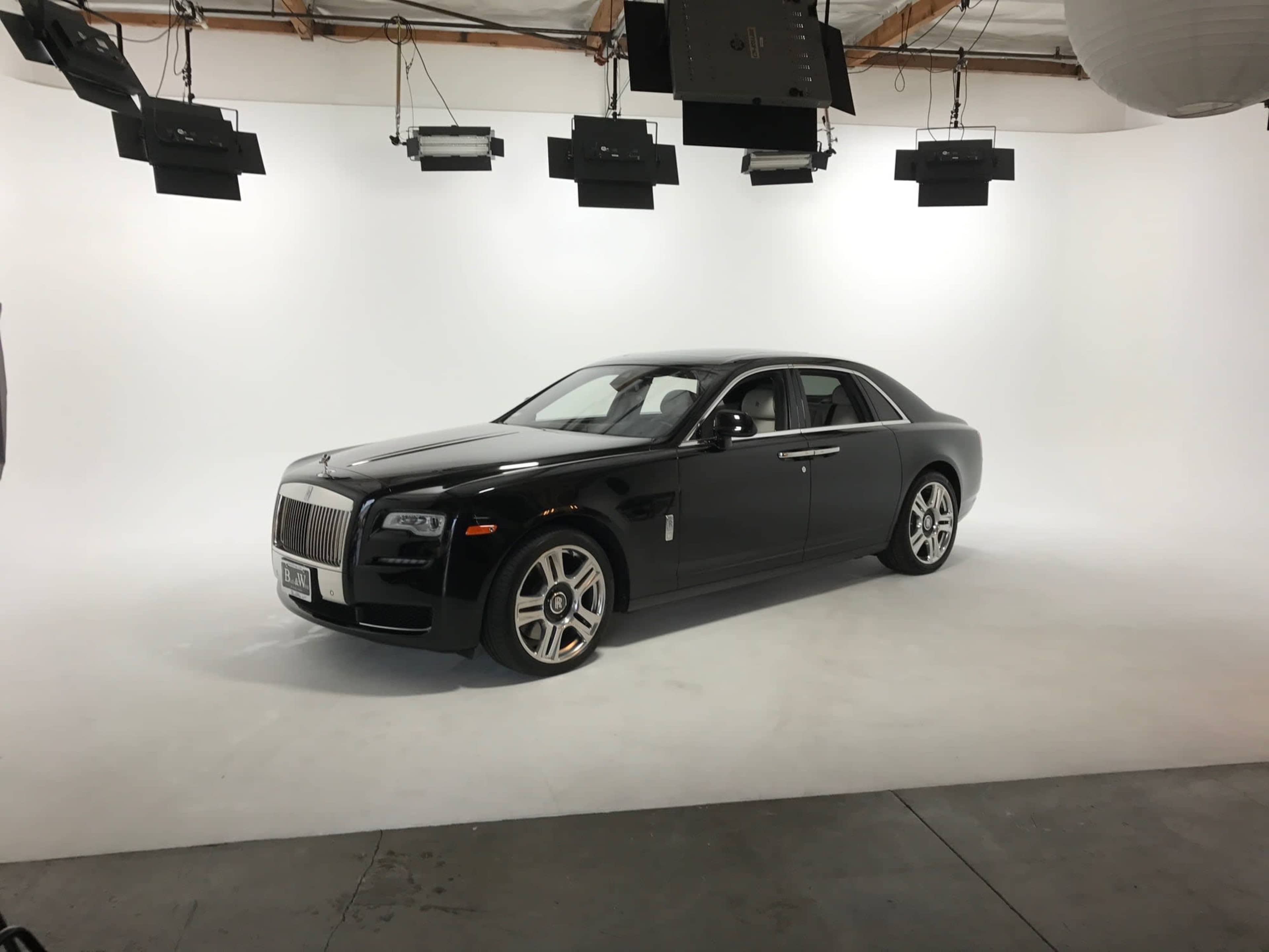 A black Rolls-Royce sedan is positioned on a seamless white backdrop under multiple studio lights.