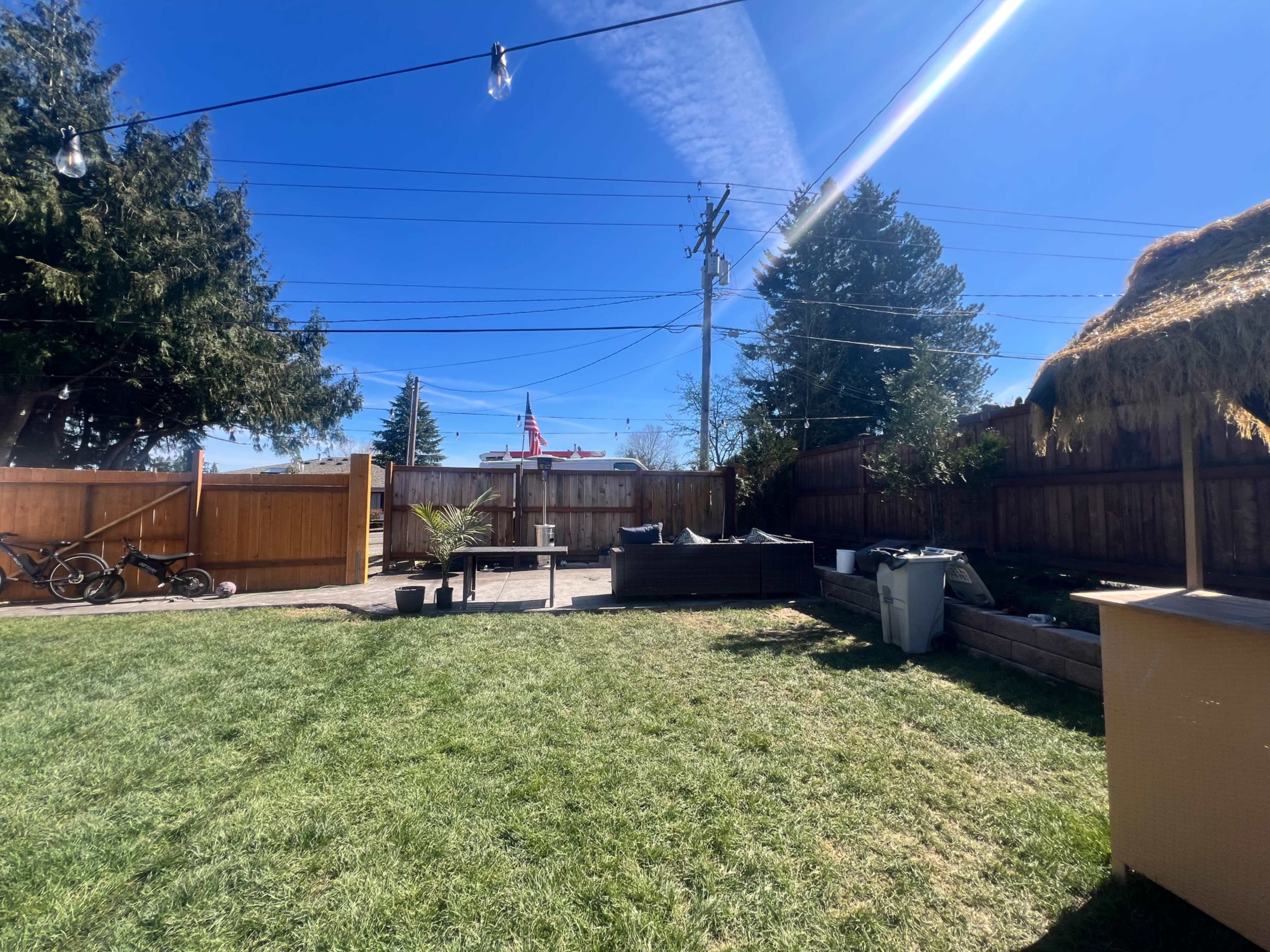 The image shows a backyard with green grass, outdoor furniture, and a clear blue sky, featuring utility poles in the background.