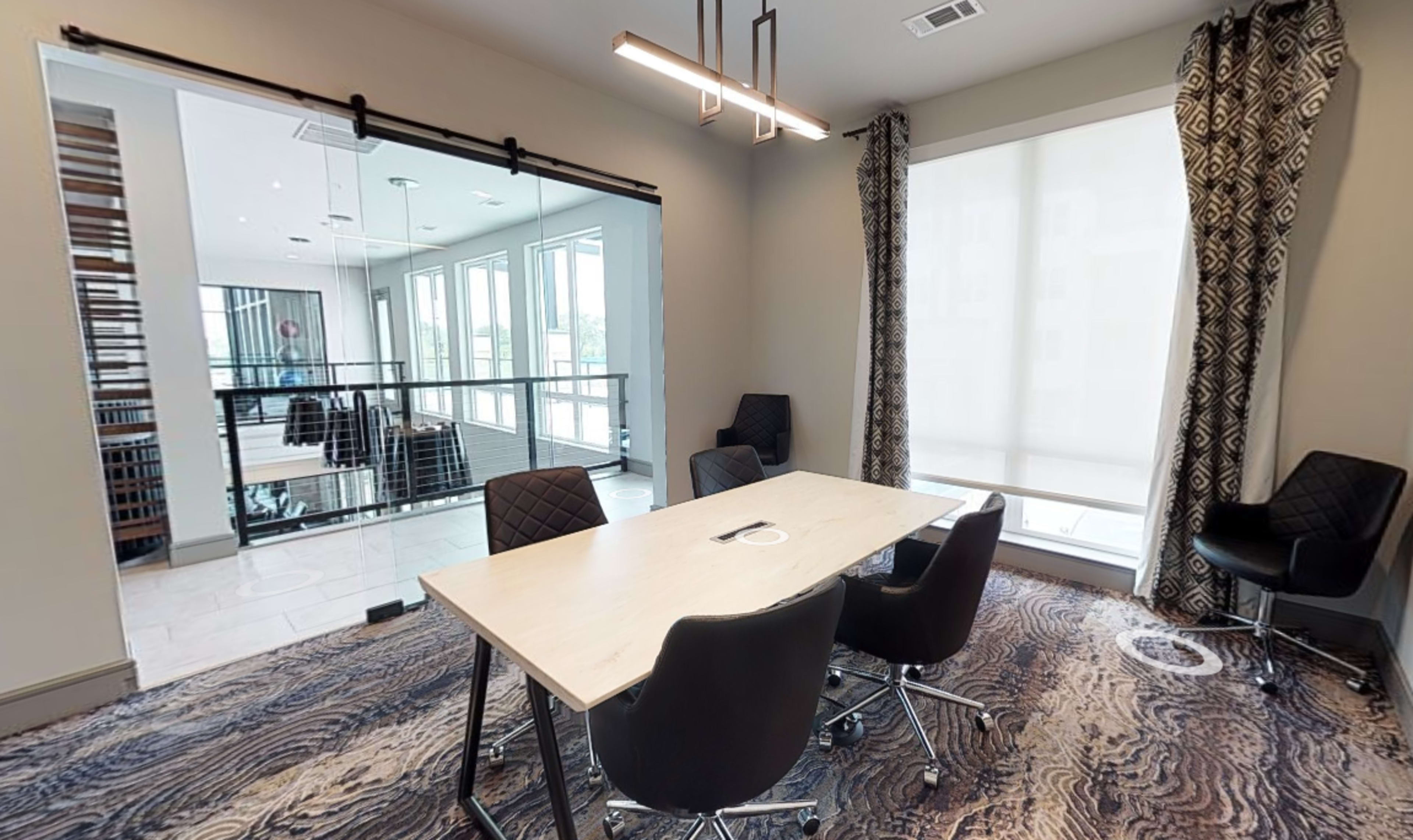 A modern conference room features a table surrounded by black chairs, with a glass partition leading to a bright, open space.