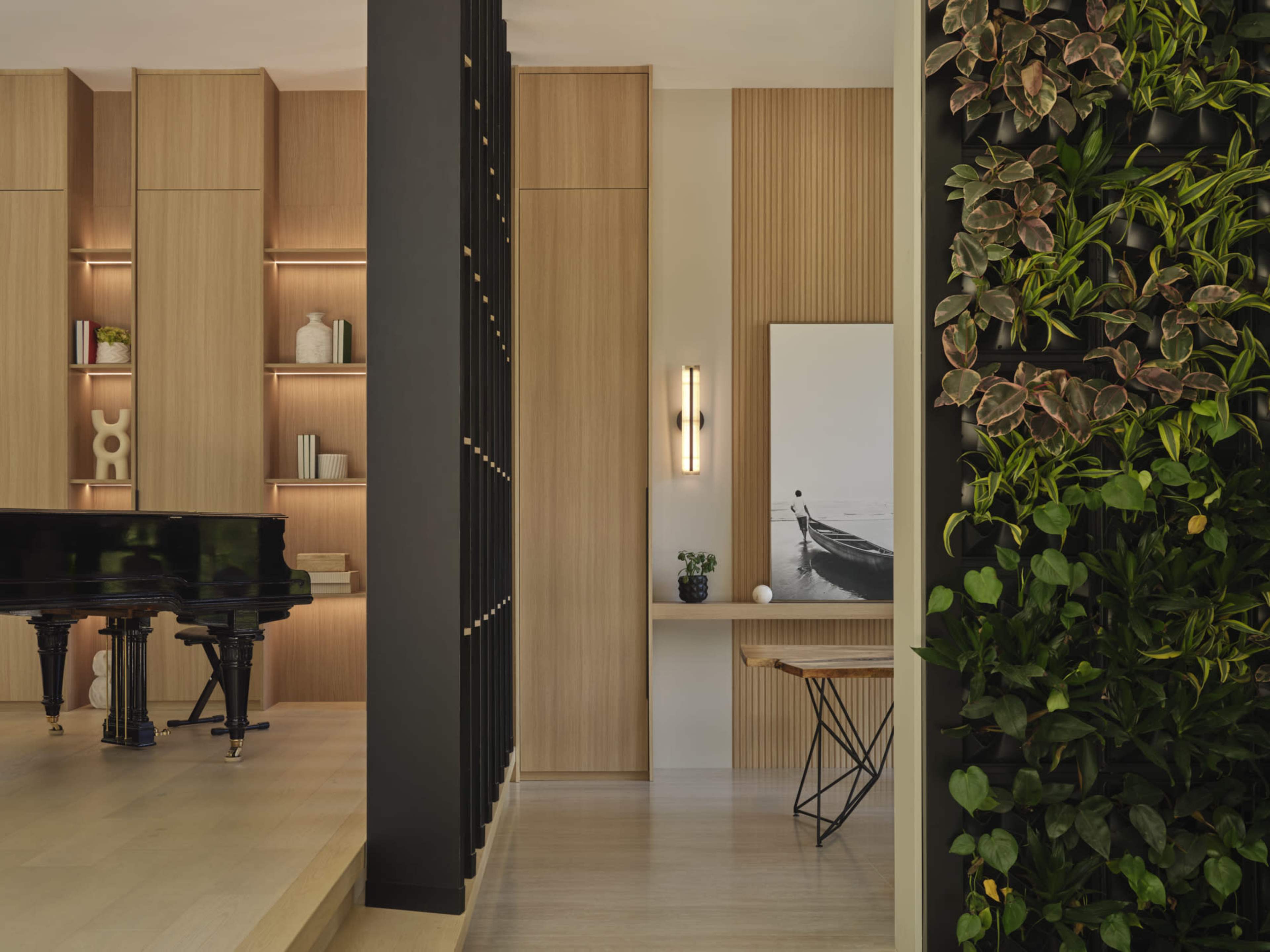 The image shows a modern interior featuring a black grand piano, wooden cabinetry with built-in lighting, and a vertical garden on a nearby wall.