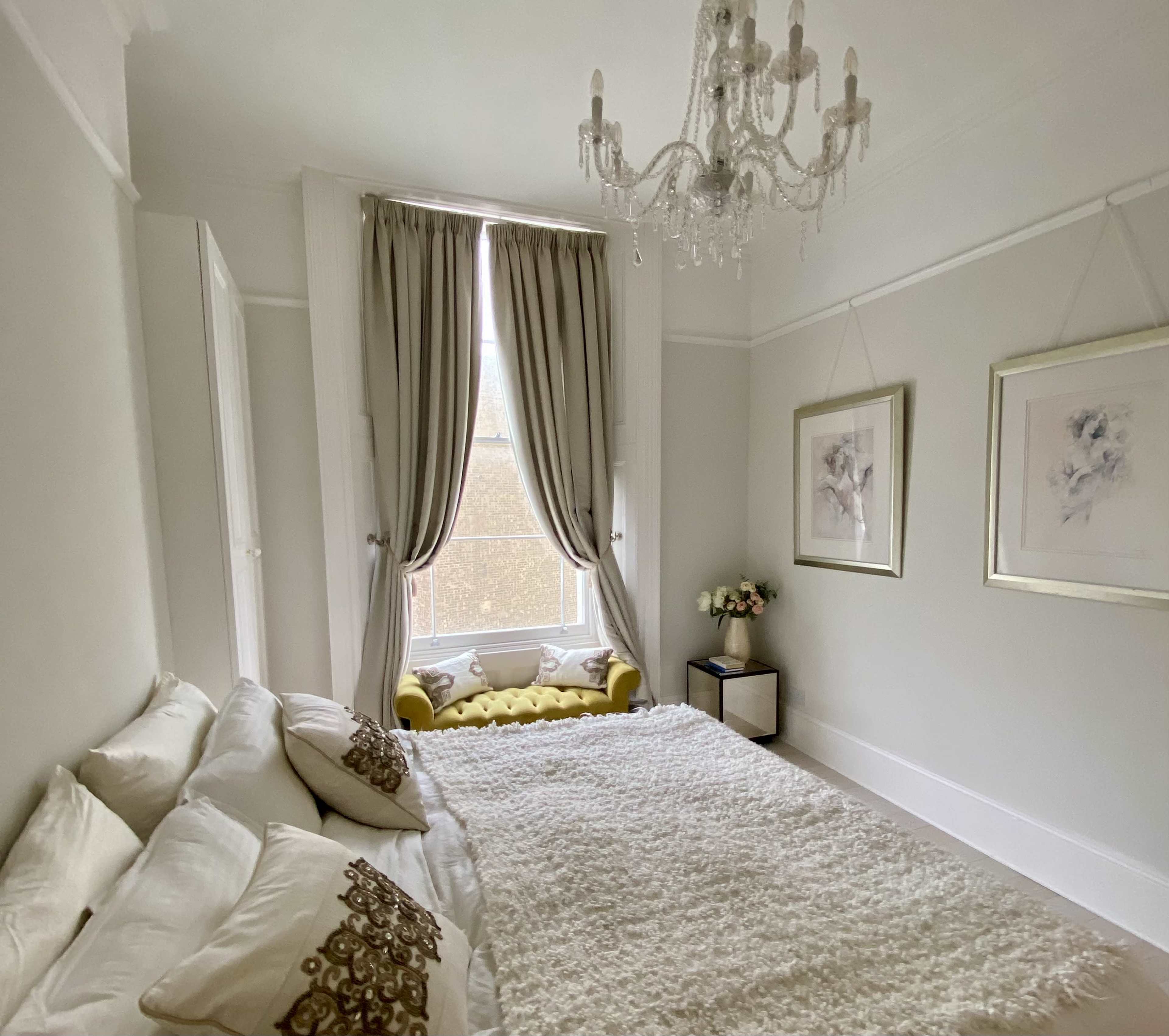 The room features a plush white rug, elegant drapes framing a large window, and framed artwork on the walls.