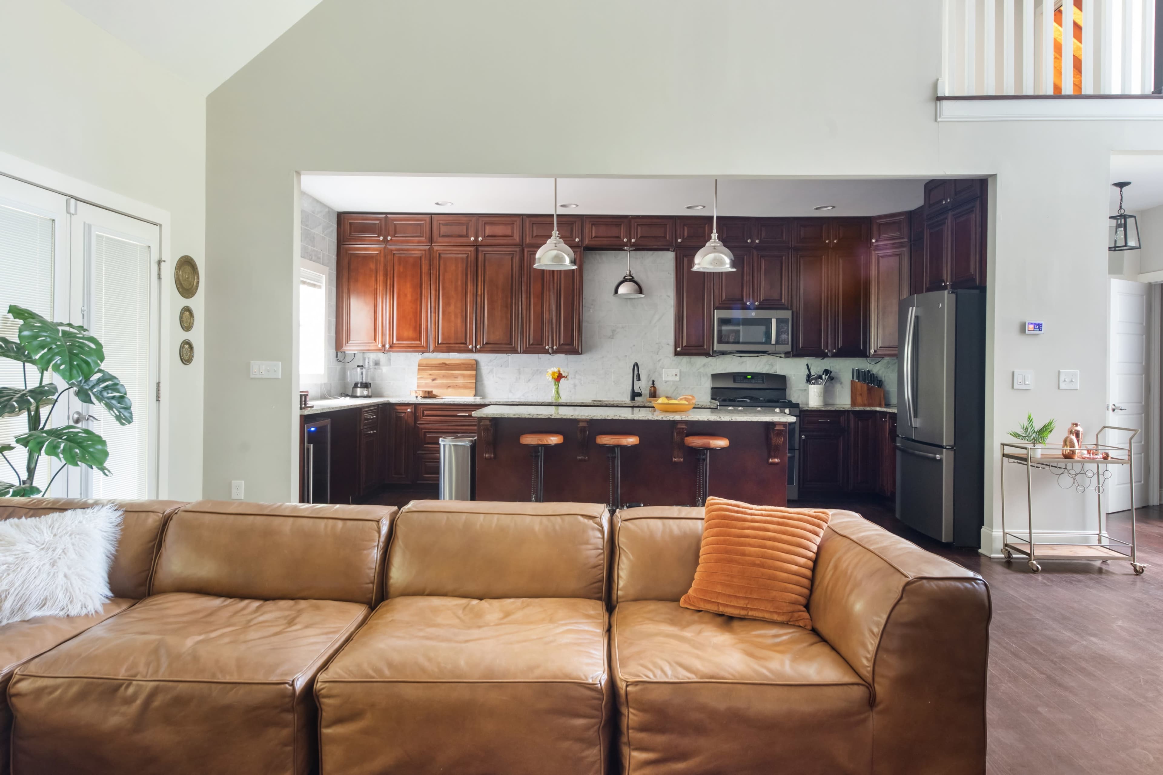 The image features a modern, open-concept kitchen with dark wooden cabinets, stainless steel appliances, and a living area furnished with a leather couch.