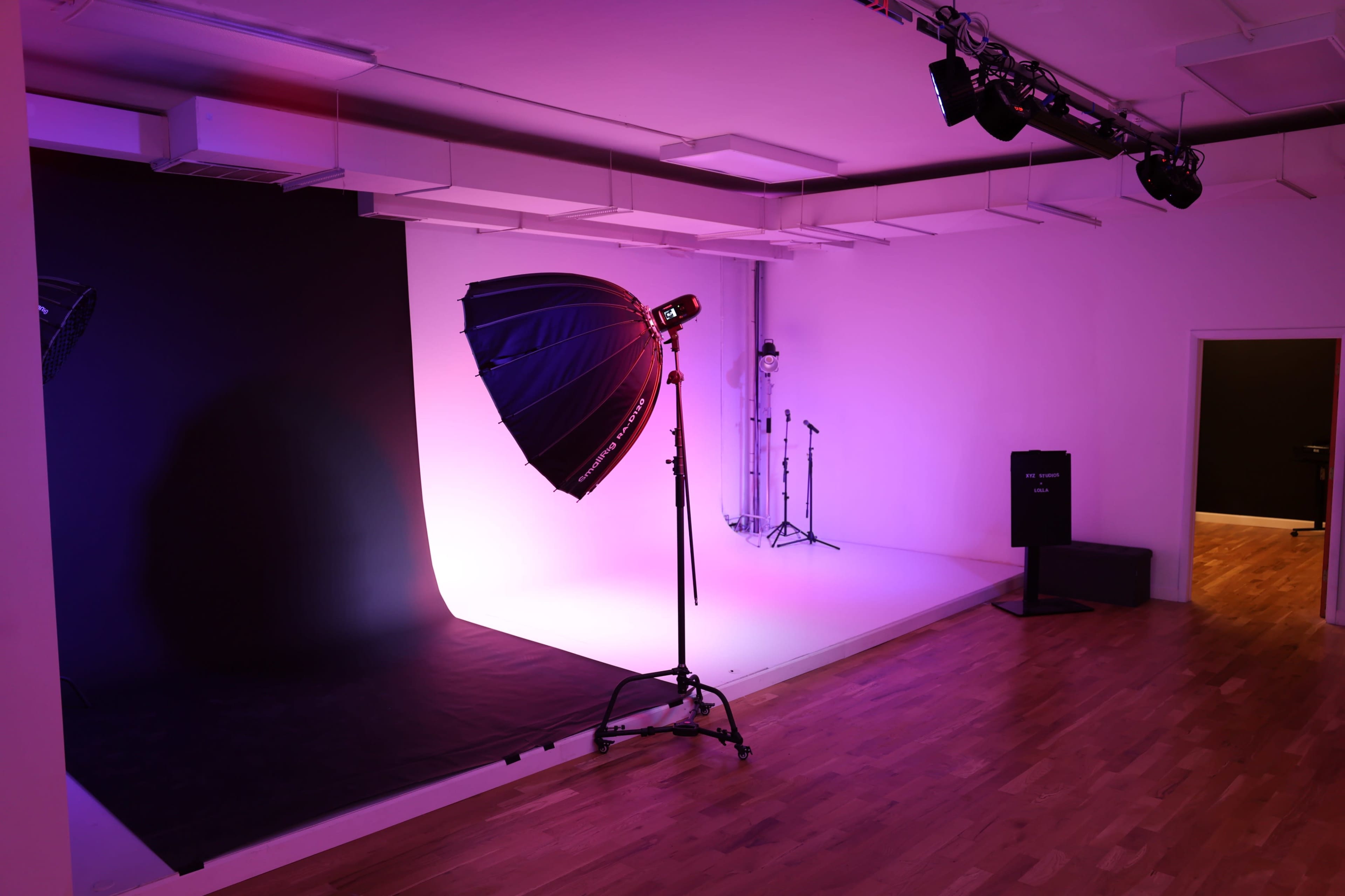 The image shows a photography studio featuring a large softbox light on a stand, a backdrop with gradient lighting, and various equipment arranged in the space.