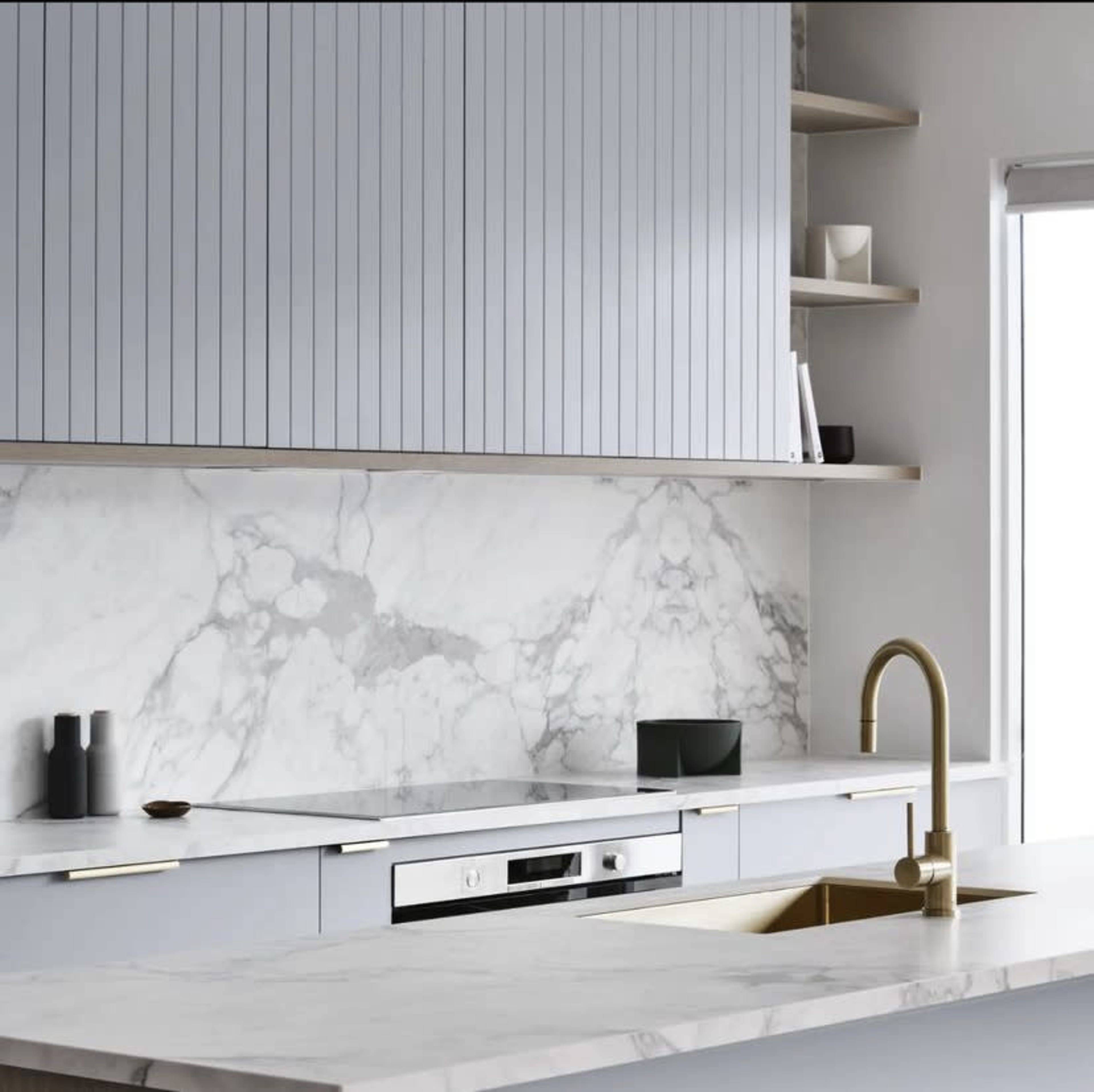 A modern kitchen features light blue cabinetry, a marble backsplash, a gold faucet, and a minimalist design.