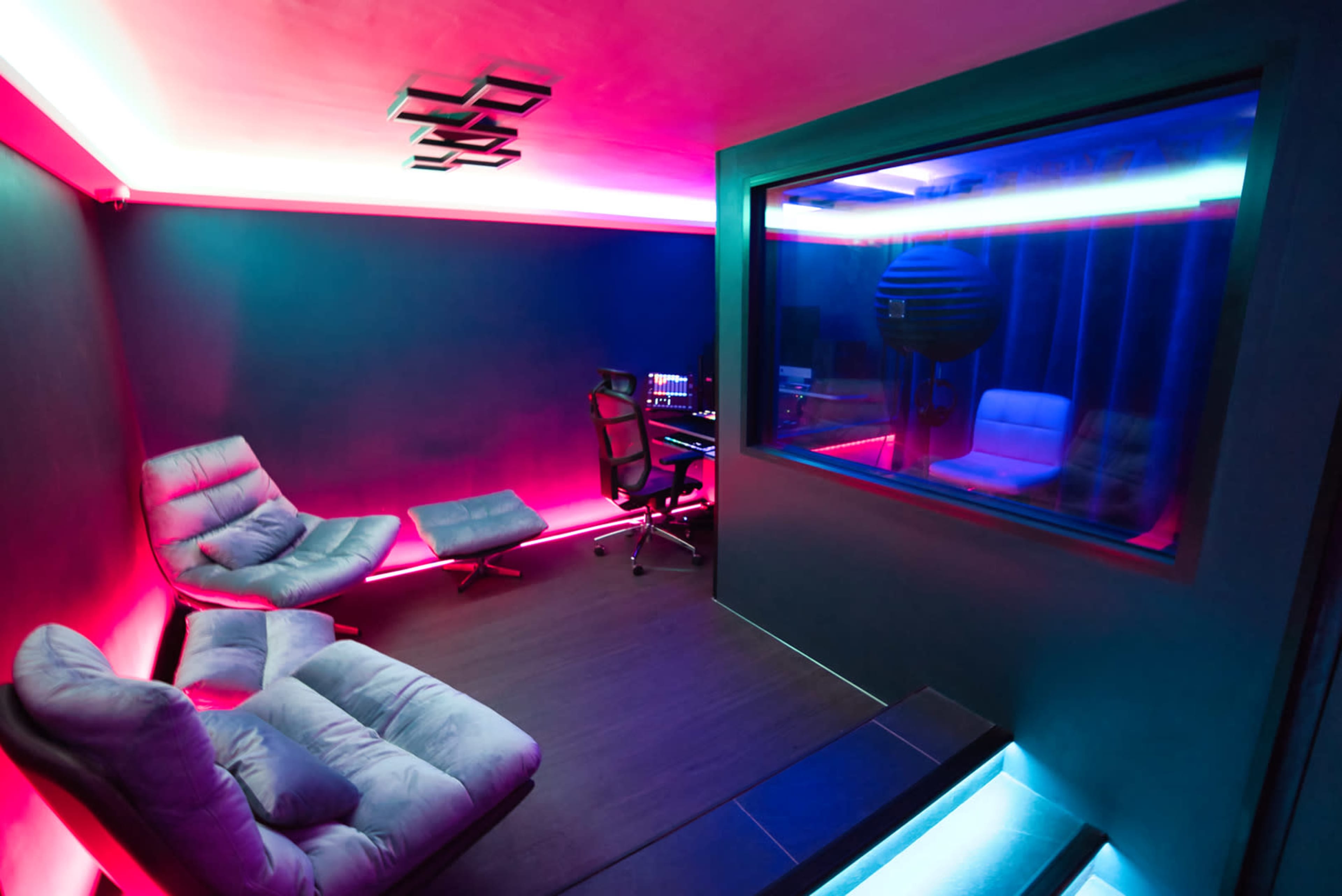 A modern recording studio with sleek furniture, LED lighting, and a glass sound booth.