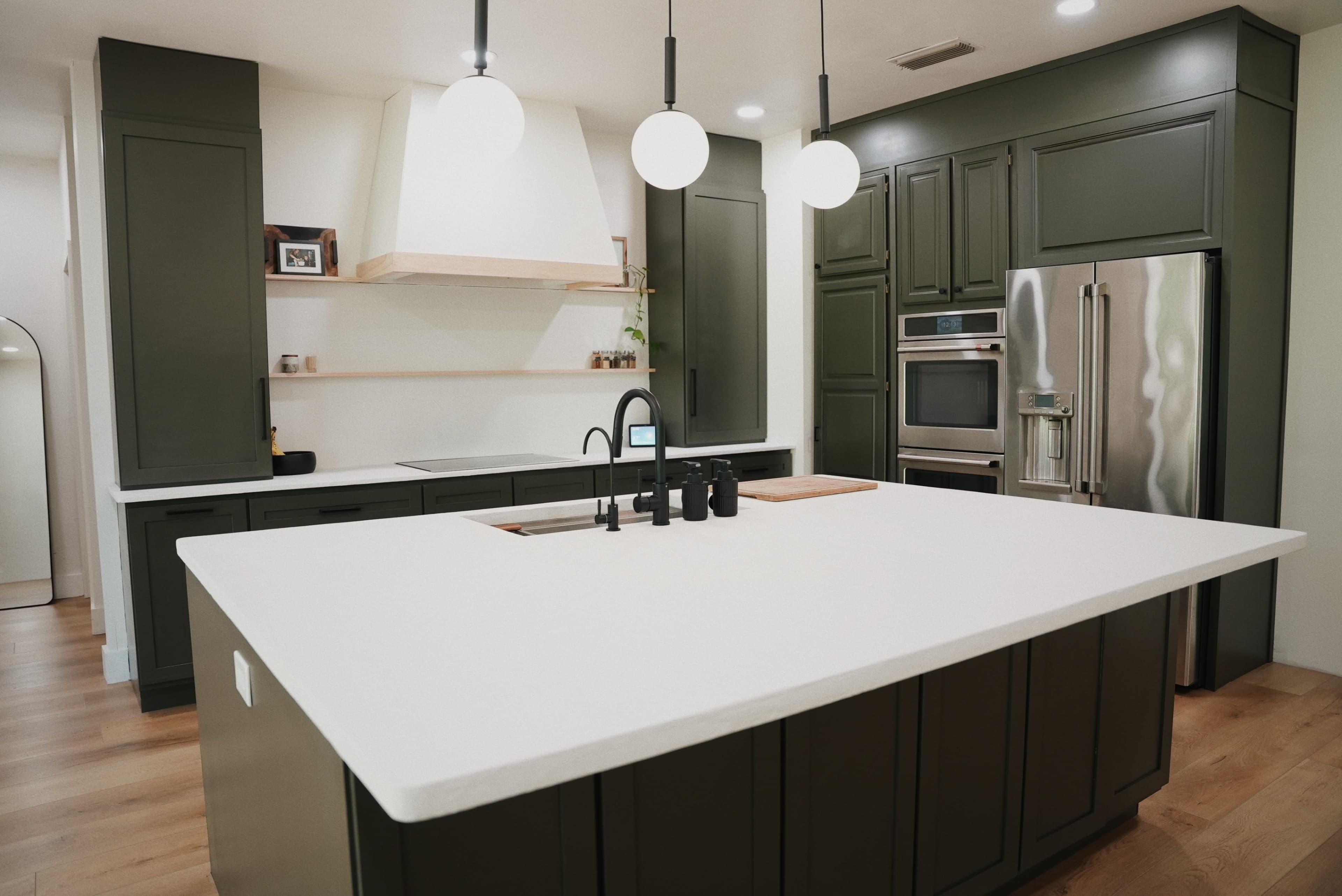 A modern kitchen features dark green cabinetry, a large white countertop, and sleek appliances.