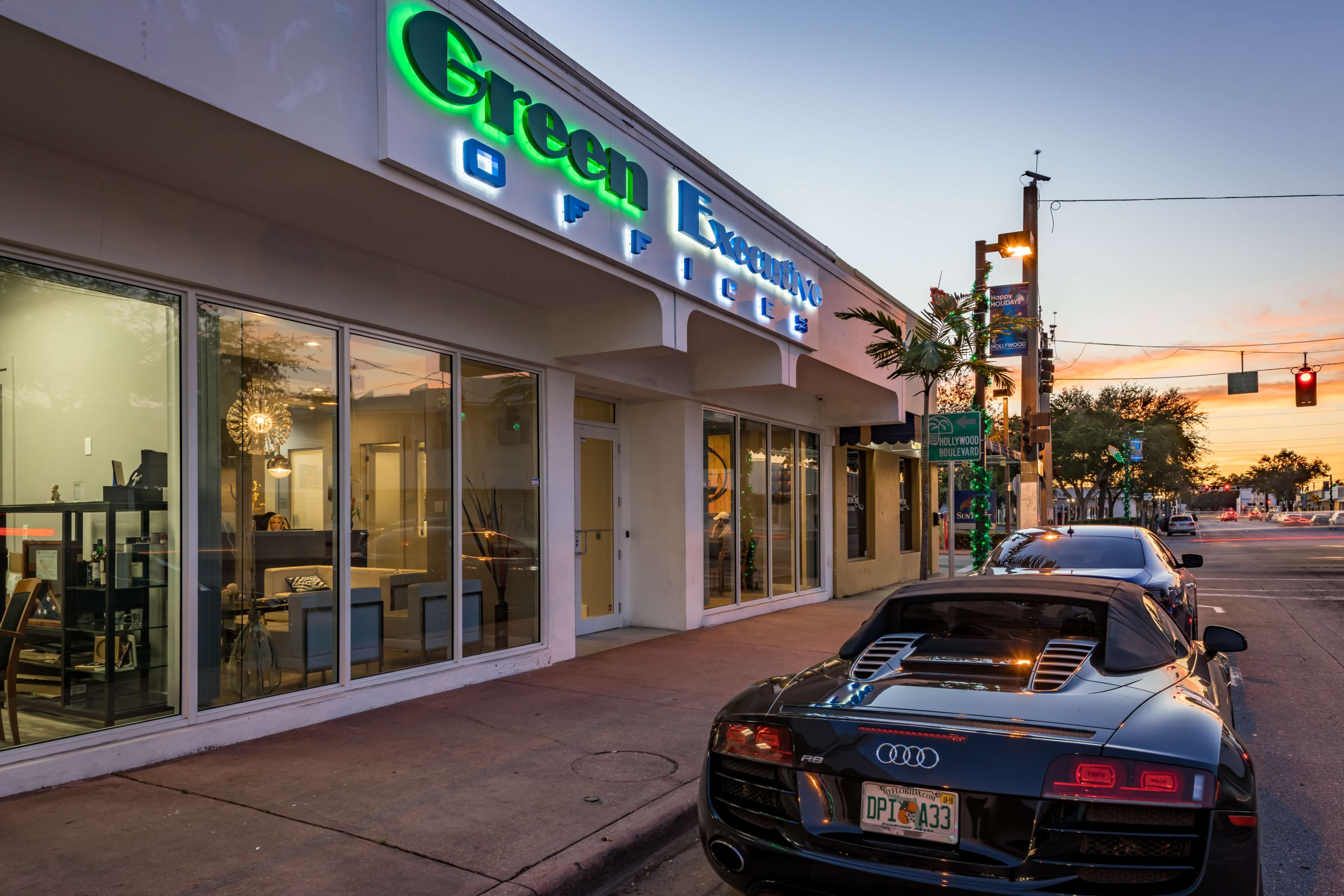 The image shows a modern office building with neon signage reading "Green Economy Offices" and an Audi sports car parked along the street.