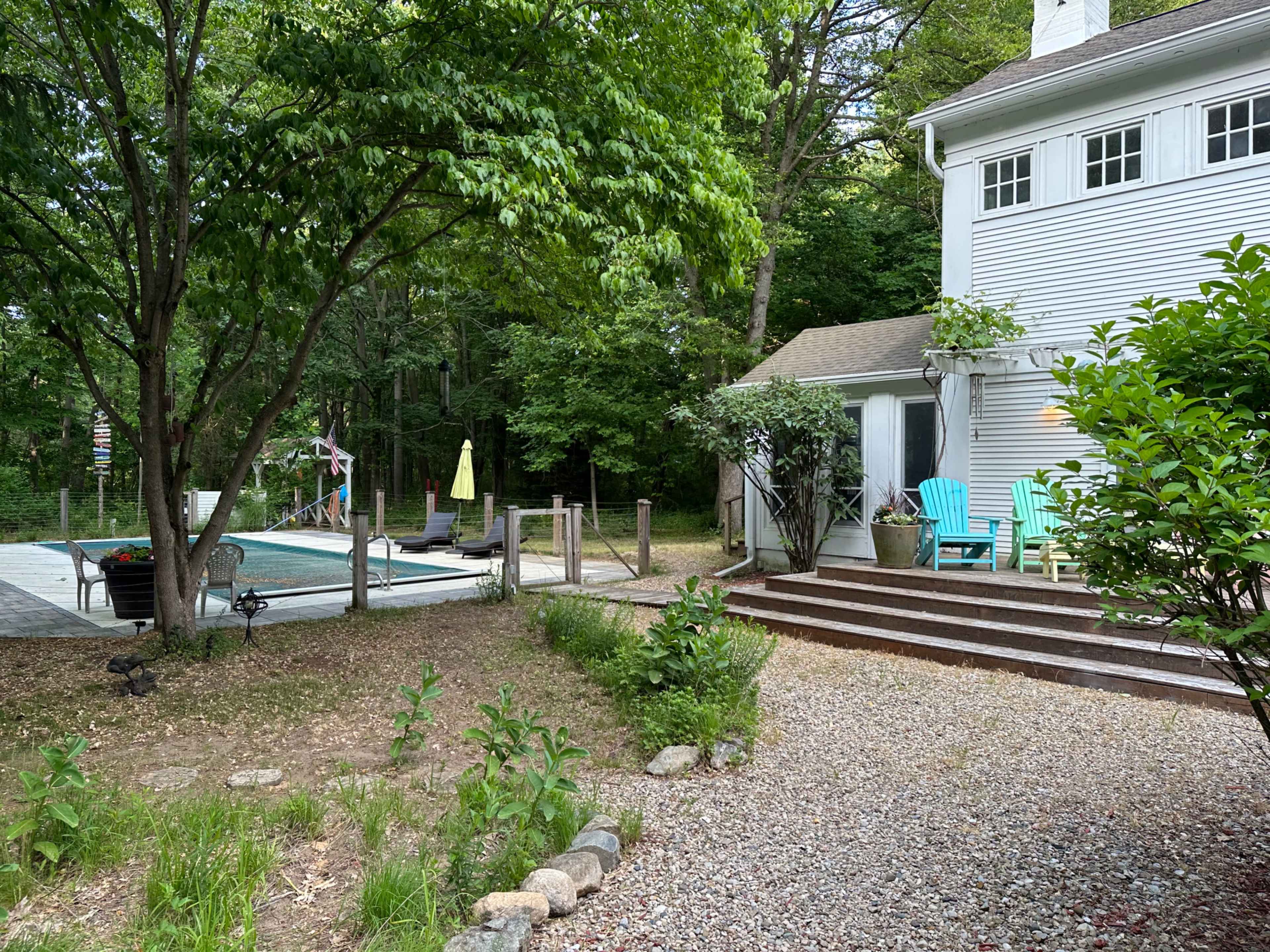A backyard area with a pool, lounge chairs, and steps leading up to a white house surrounded by greenery.