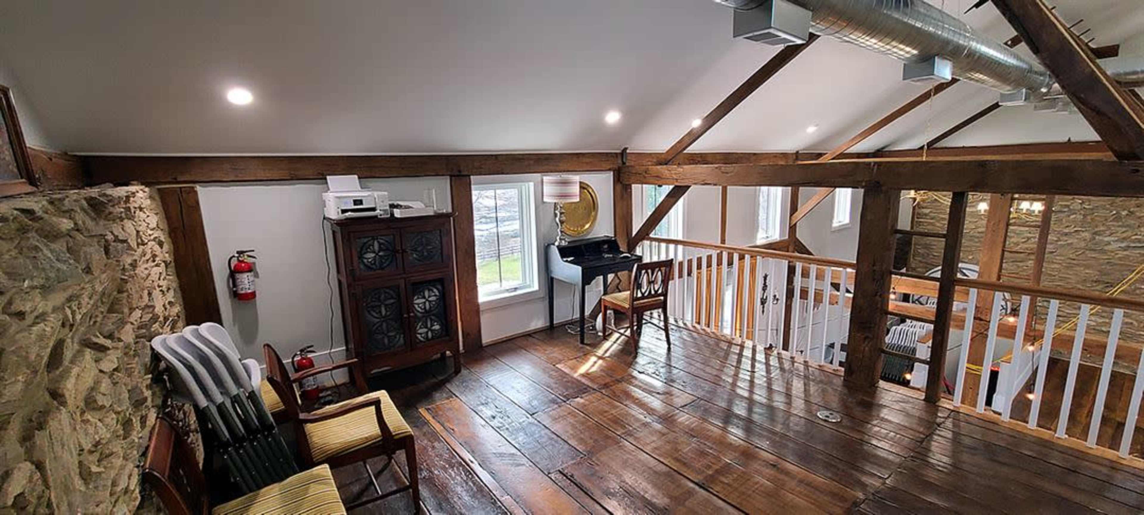 The image shows a loft area with wooden beams, a piano, and a mix of seating and decorative elements.