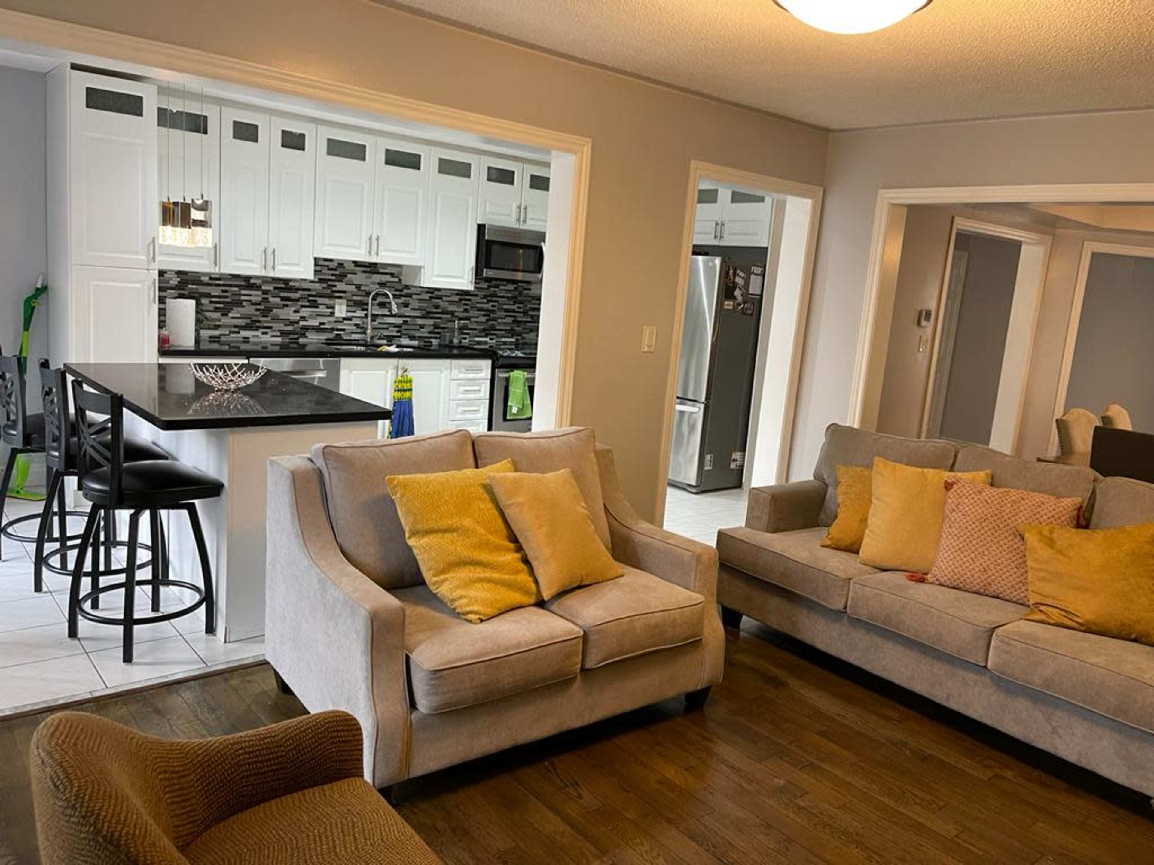 A living room with two gray sofas, a coffee table, and an open kitchen area in the background featuring white cabinetry and a black countertop.