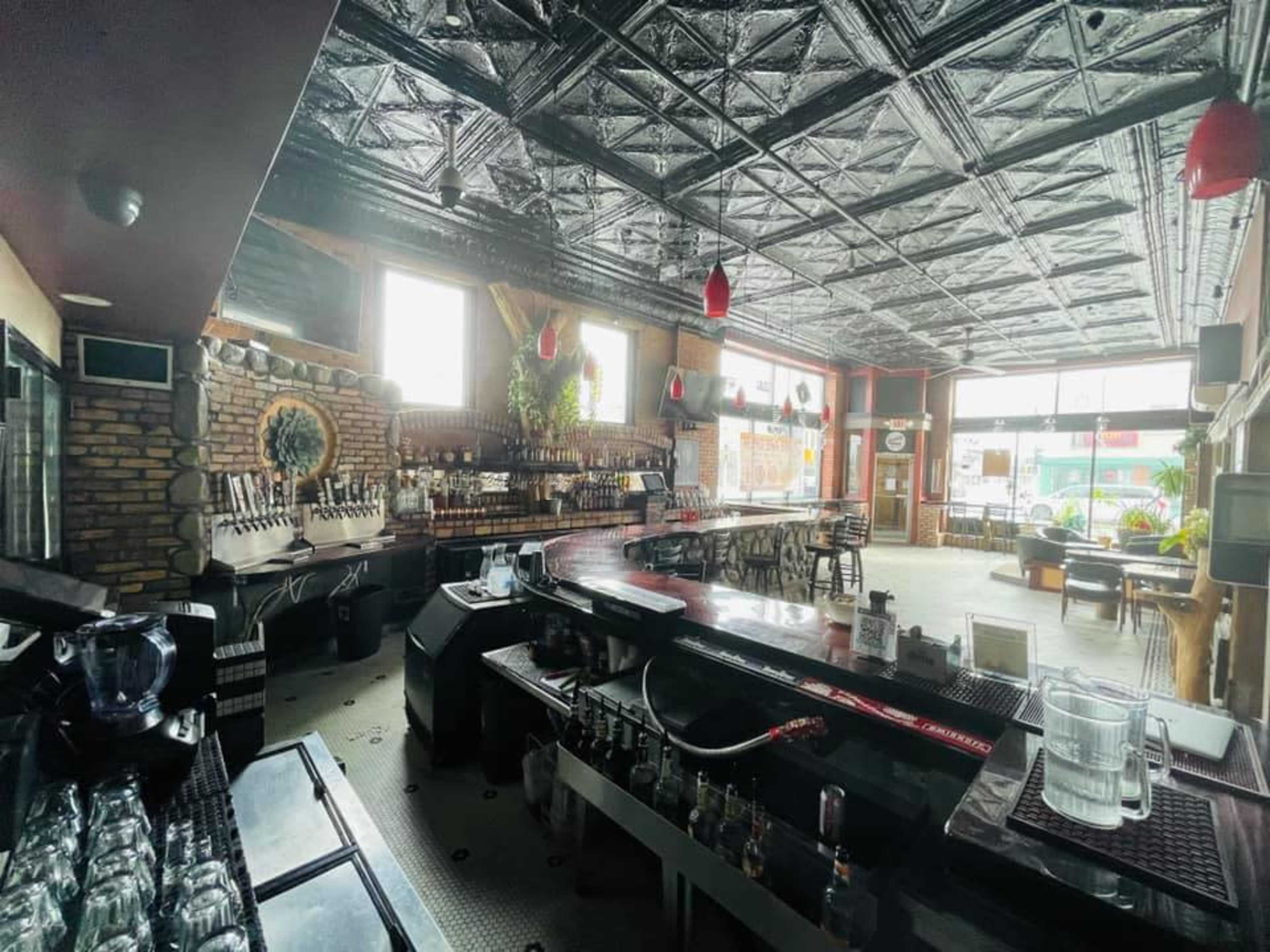 An empty bar interior with a curved counter, various beer taps, and a seating area featuring tables and chairs.