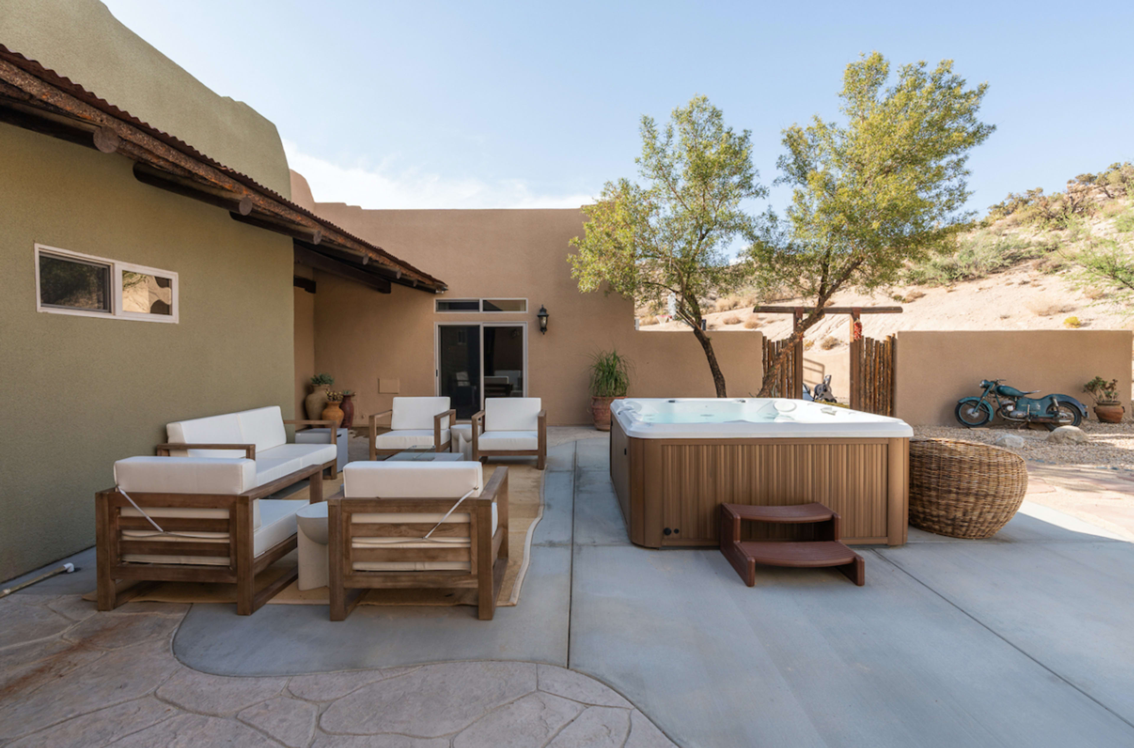 The image shows a backyard patio with a hot tub, seating area, and desert landscape in the background.