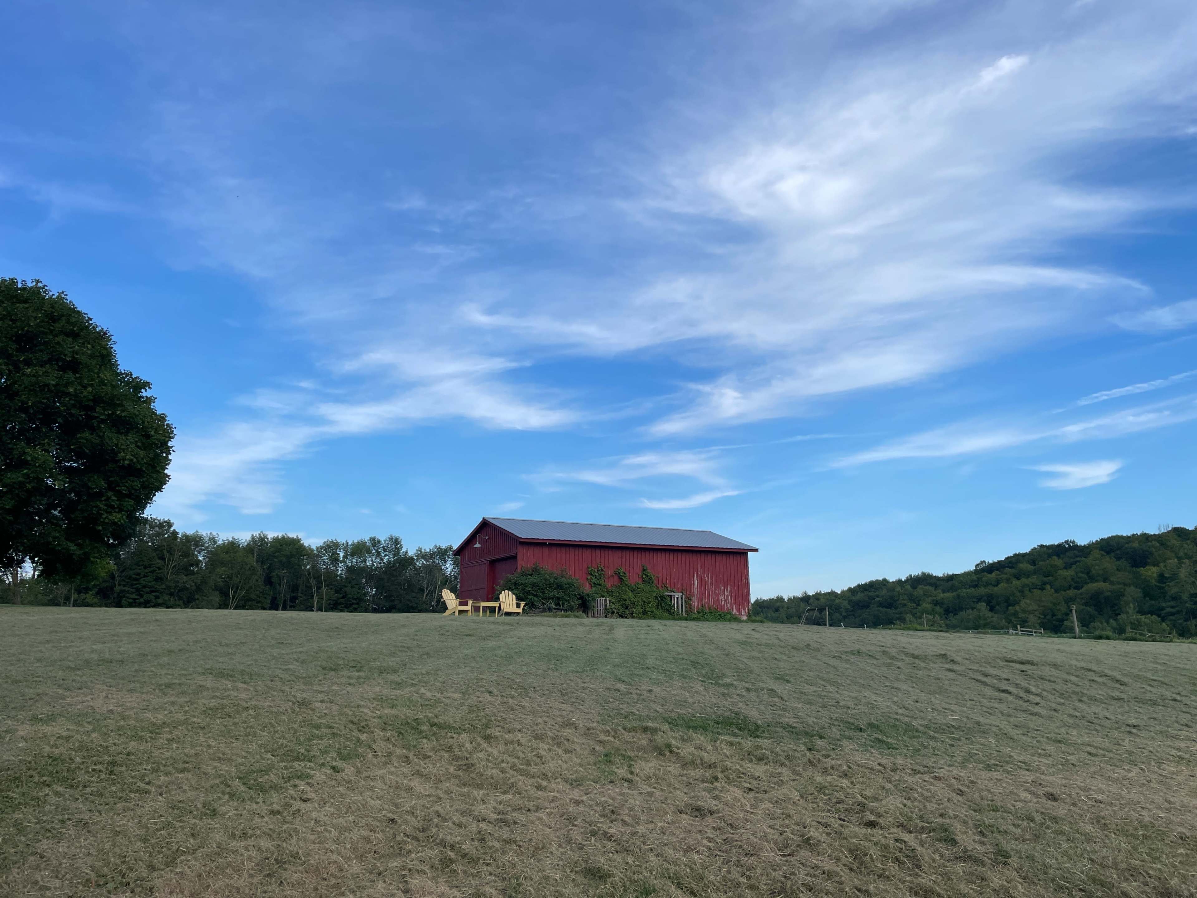 A red barn sits on a grassy hillside beneath a blue sky with wispy clouds.