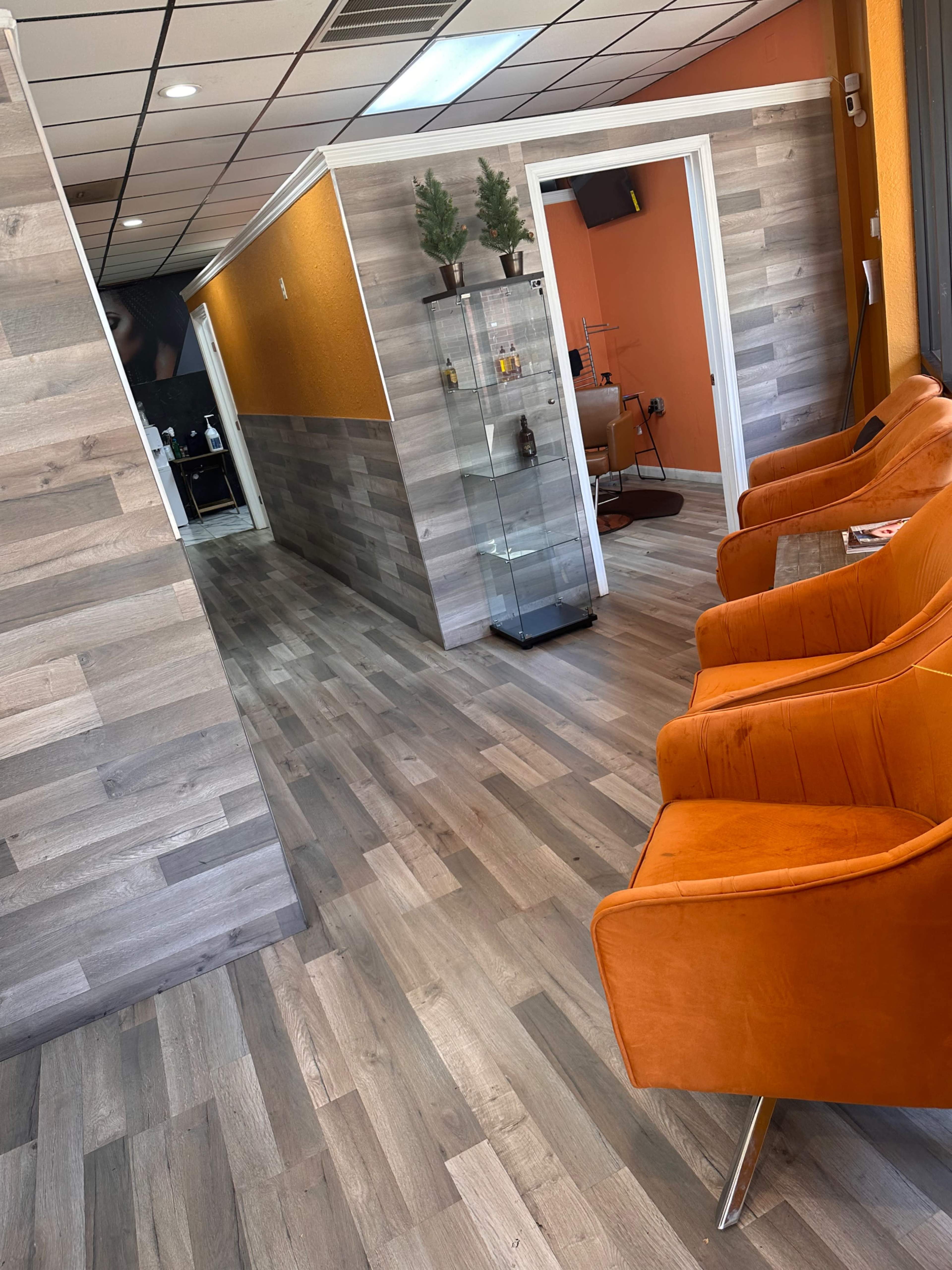 A modern waiting area with orange accent walls, gray wood flooring, and vibrant orange chairs arranged near a wall with a glass display case.
