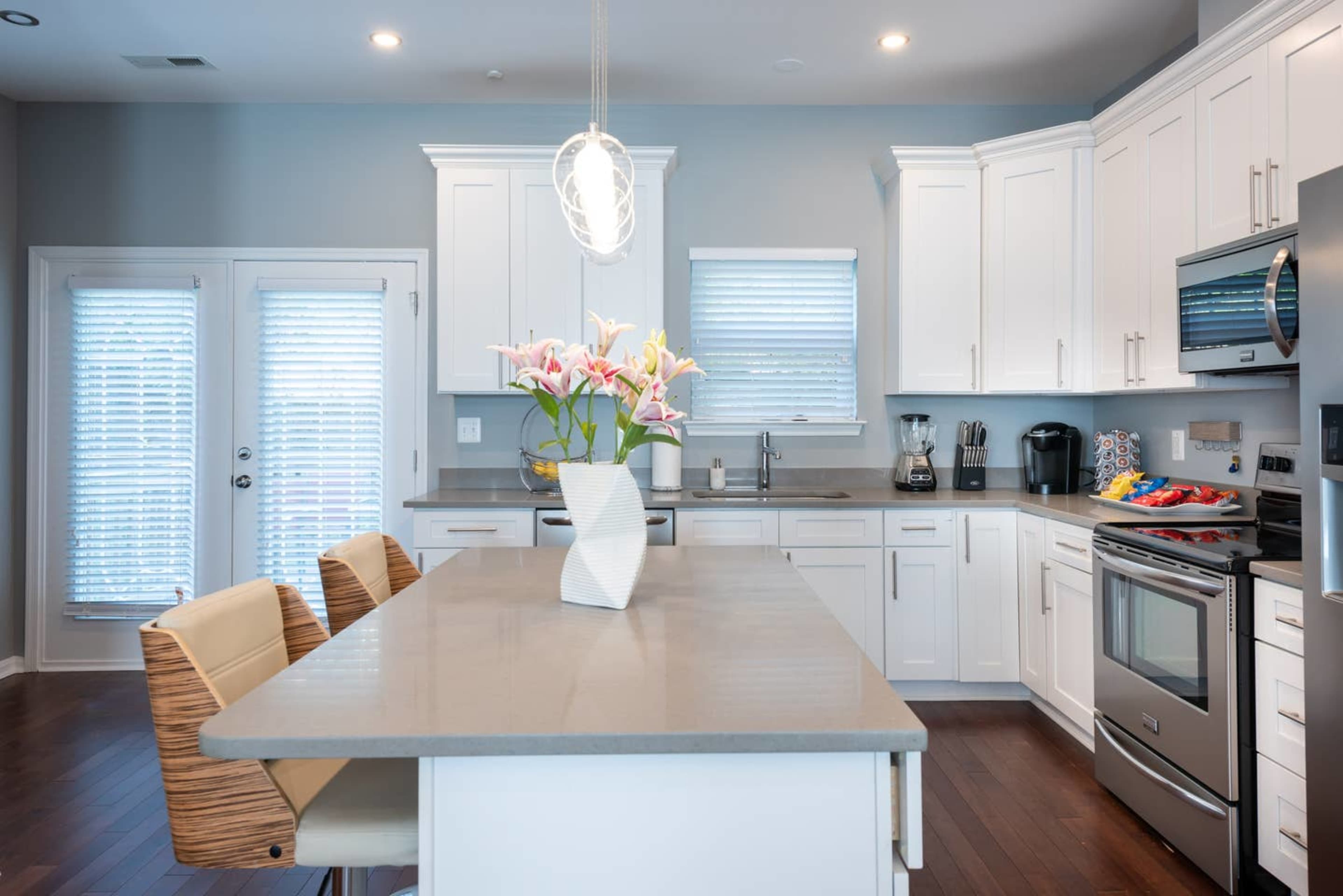 A modern kitchen features white cabinets, a gray island with a vase of flowers, and stainless steel appliances.