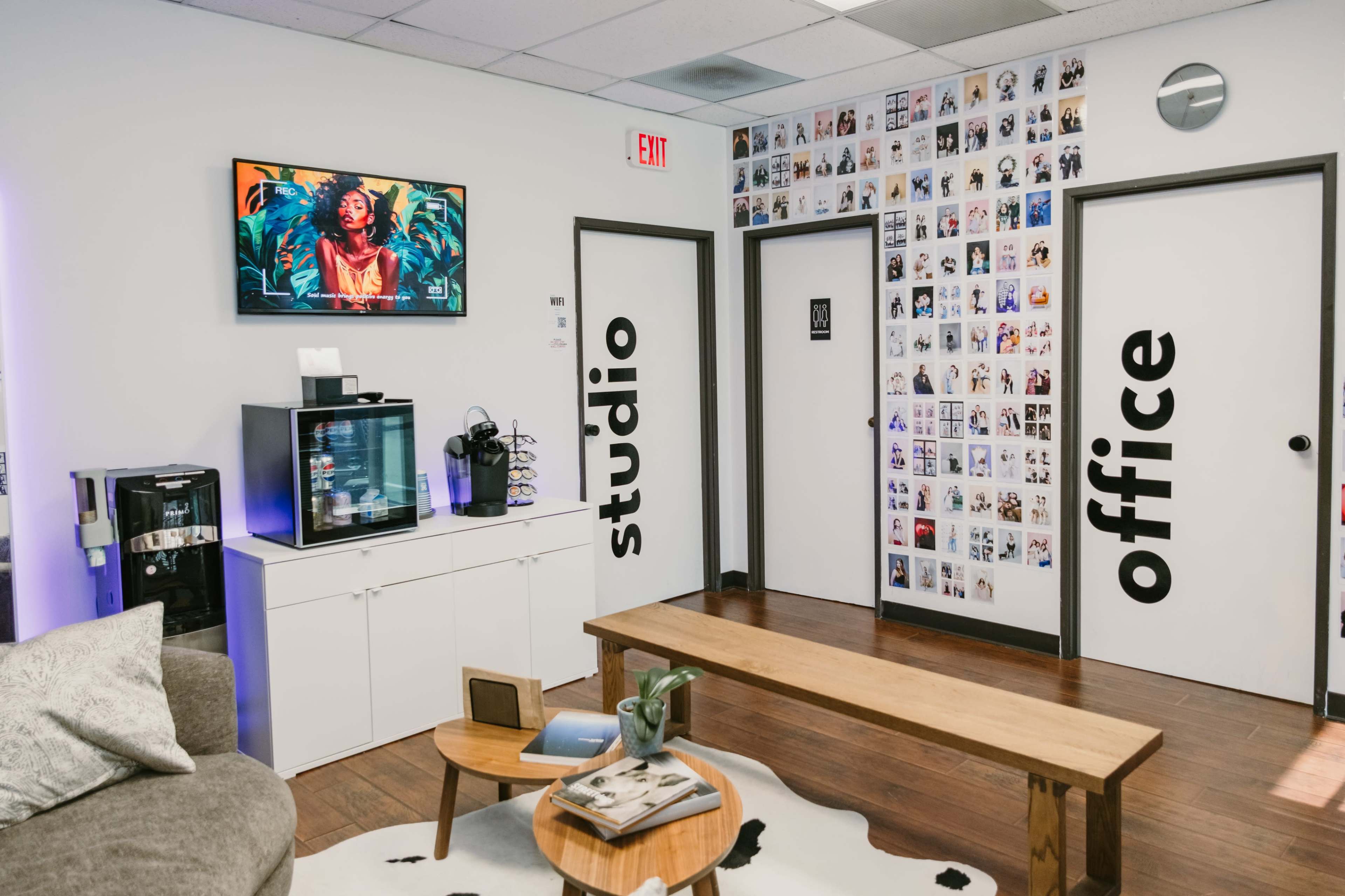 A modern office space featuring a seating area, a beverage station, and a wall decorated with photos.