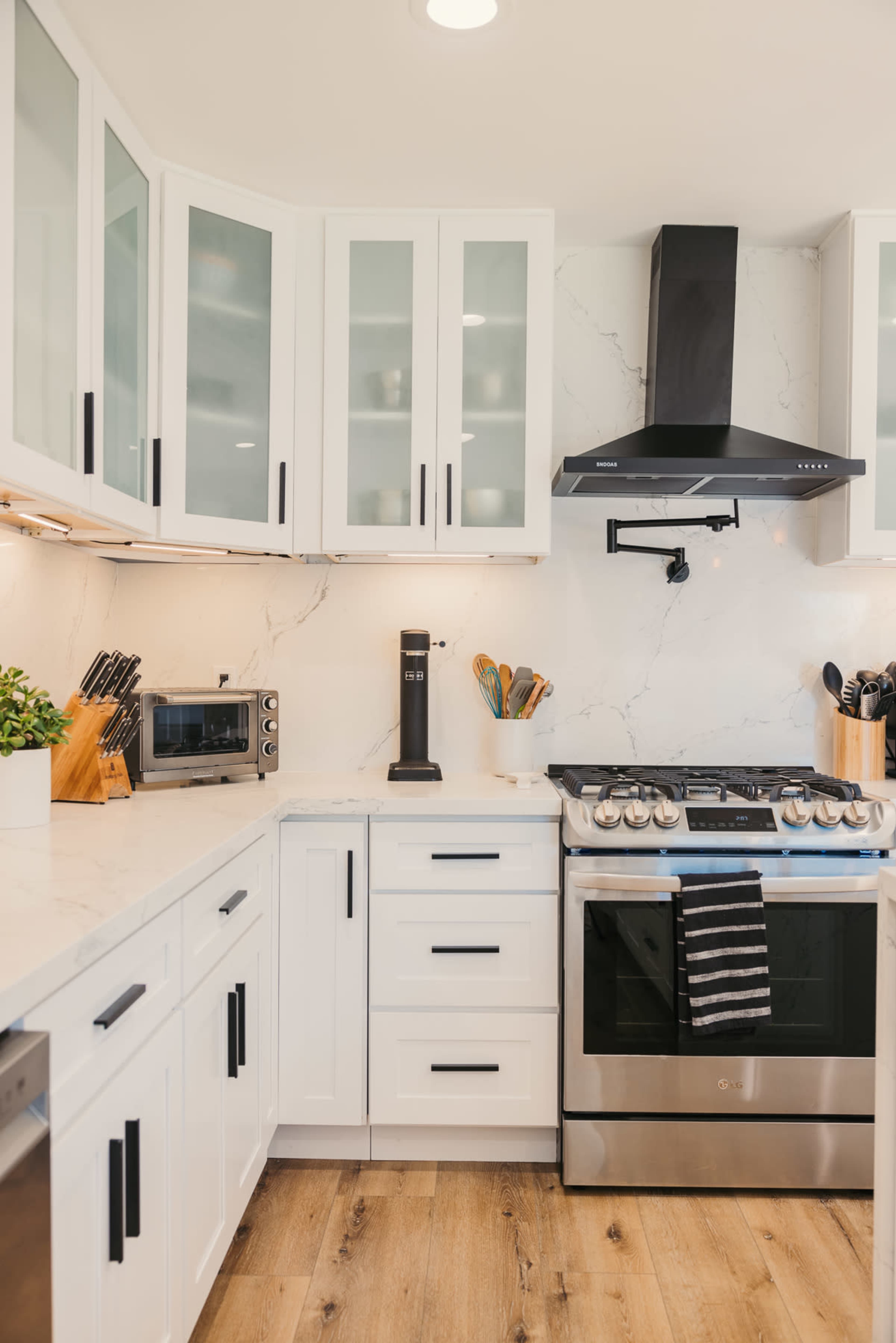 A modern kitchen featuring white cabinets, a stainless steel stove with a black hood, and a marble countertop.