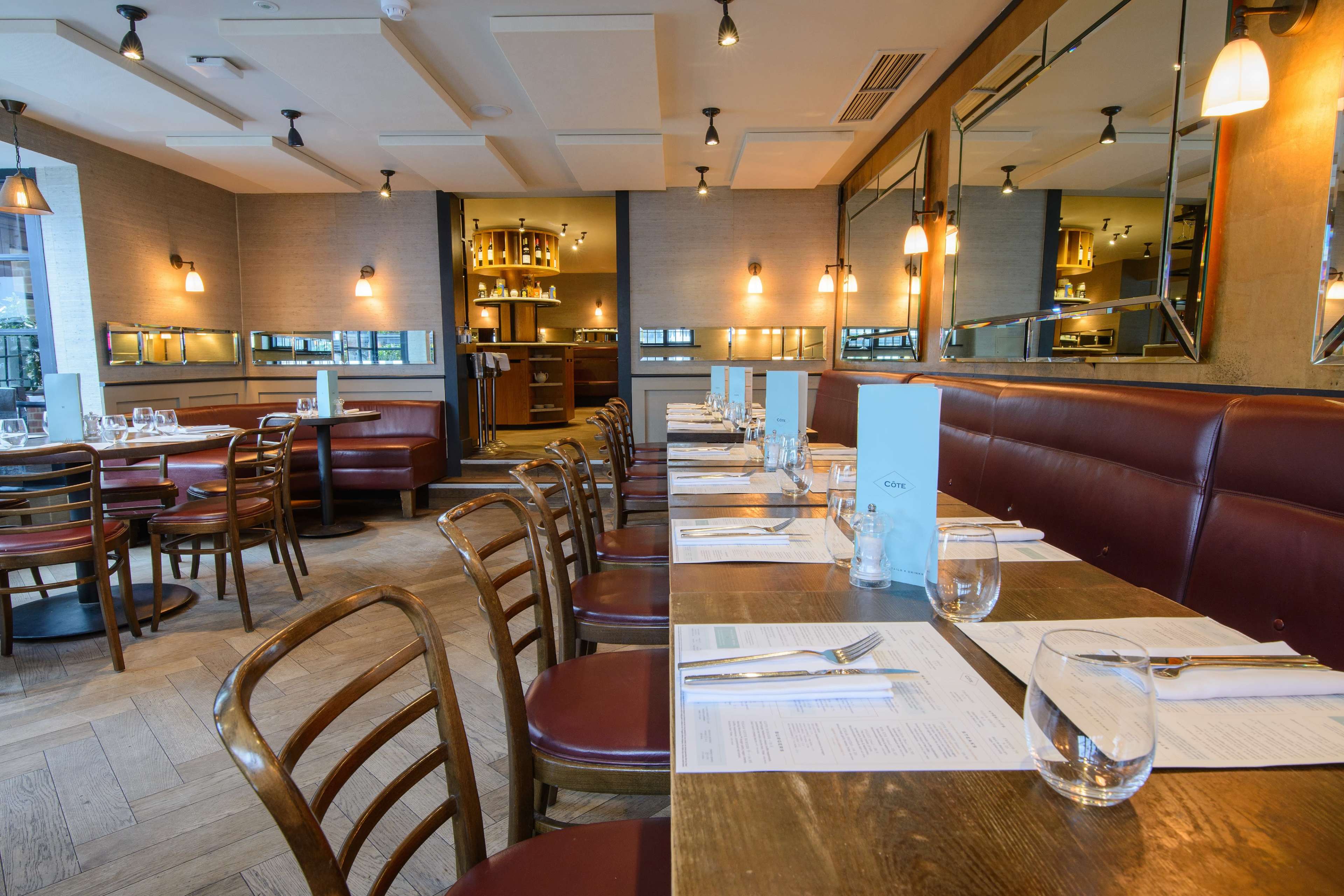 The image shows a restaurant interior with wooden tables, brown leather seating, and neatly arranged table settings.