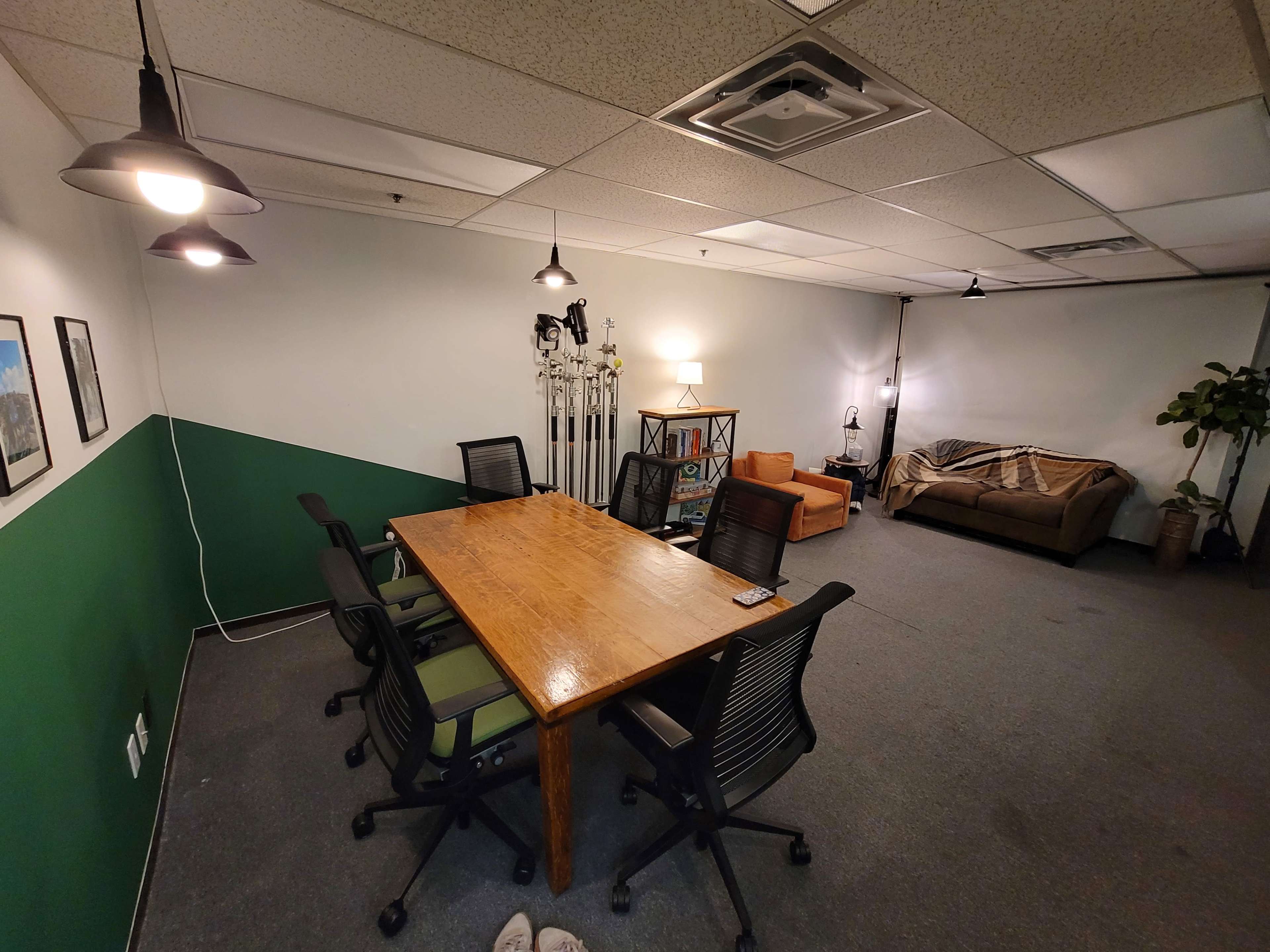 A conference room with a large wooden table surrounded by black and green office chairs, a sectional sofa in the corner, and wall decor including framed pictures.