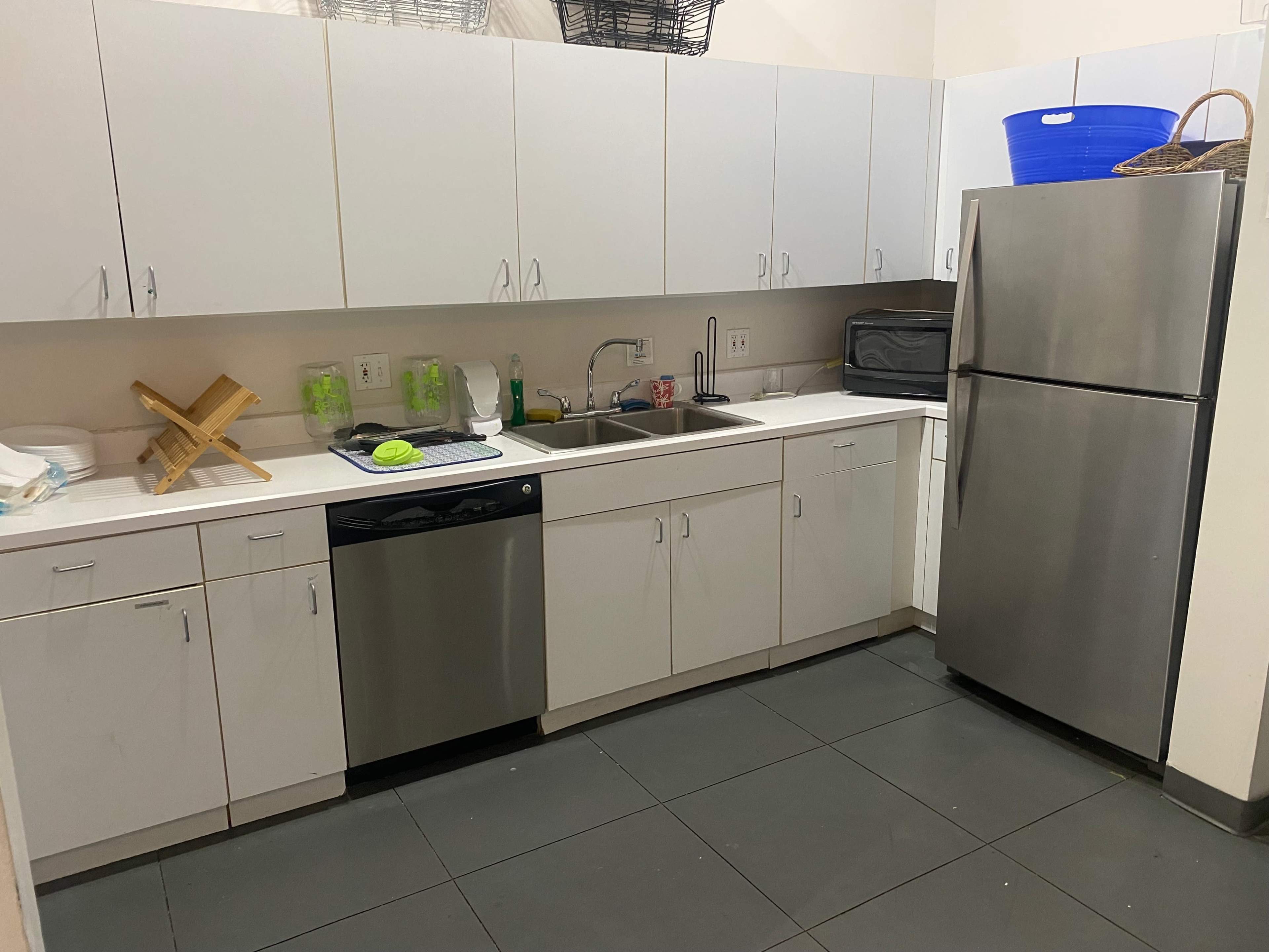 A minimalist kitchen with white cabinets, a stainless steel refrigerator, a sink, and a dishwasher, all positioned along a sleek countertop.
