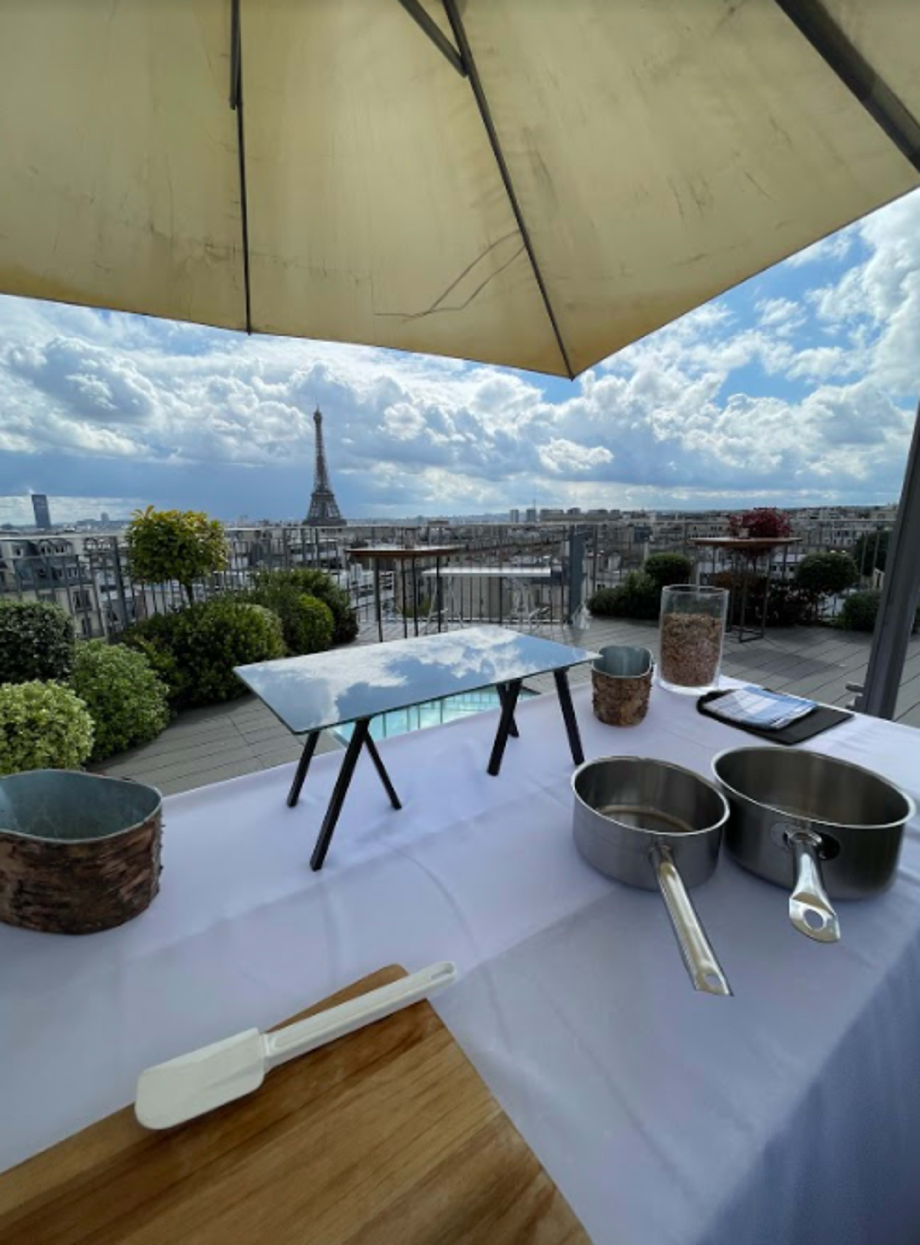 A rooftop dining setup features a table overlooking the Paris skyline with the Eiffel Tower visible in the distance.