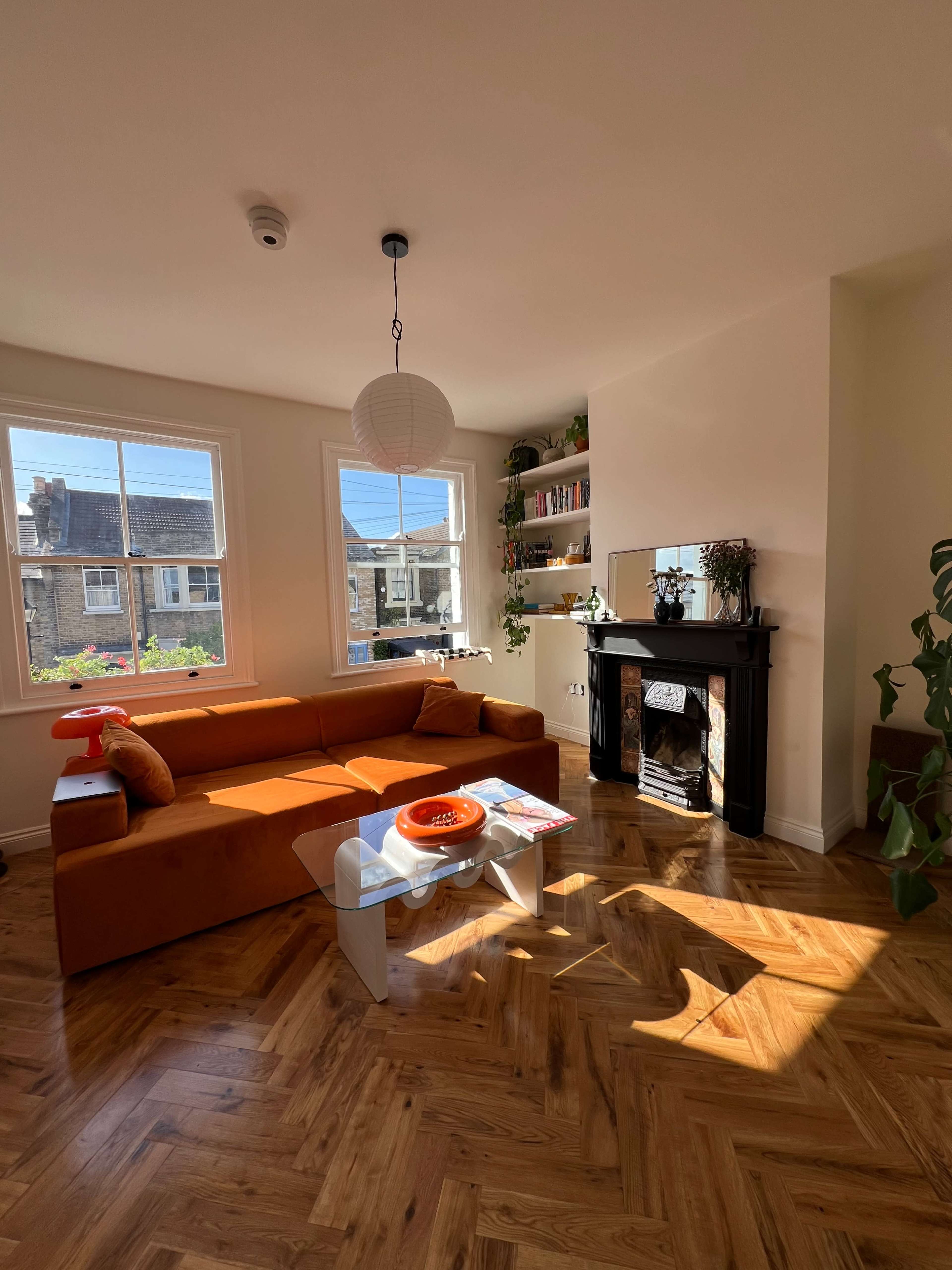 A living room features a brown sectional sofa, a glass coffee table, and a black fireplace, with natural light streaming through large windows.