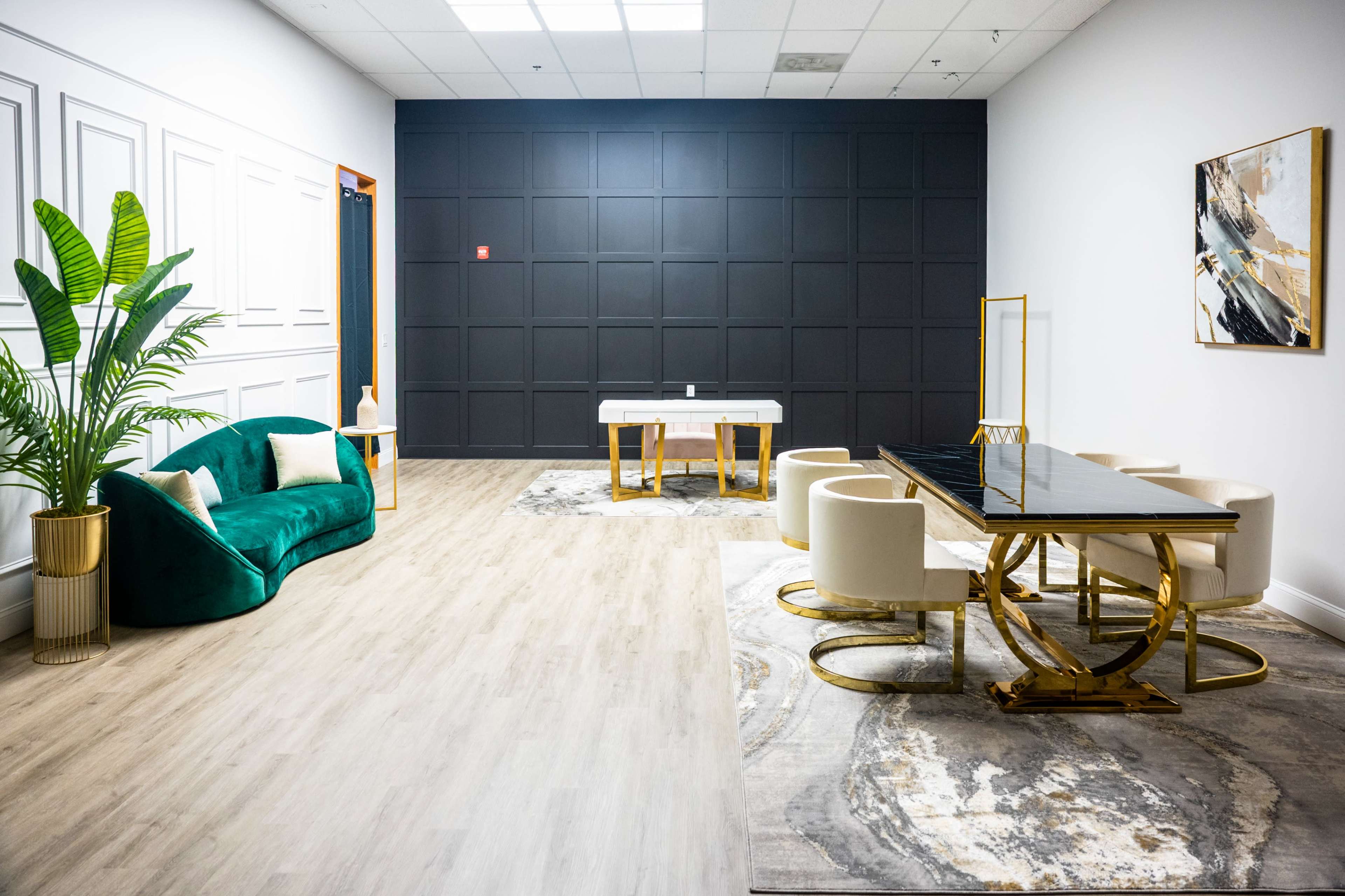 A modern interior space featuring a green velvet sofa, a white dining table, and a dining set, with a dark textured wall and a decorative plant in the corner.
