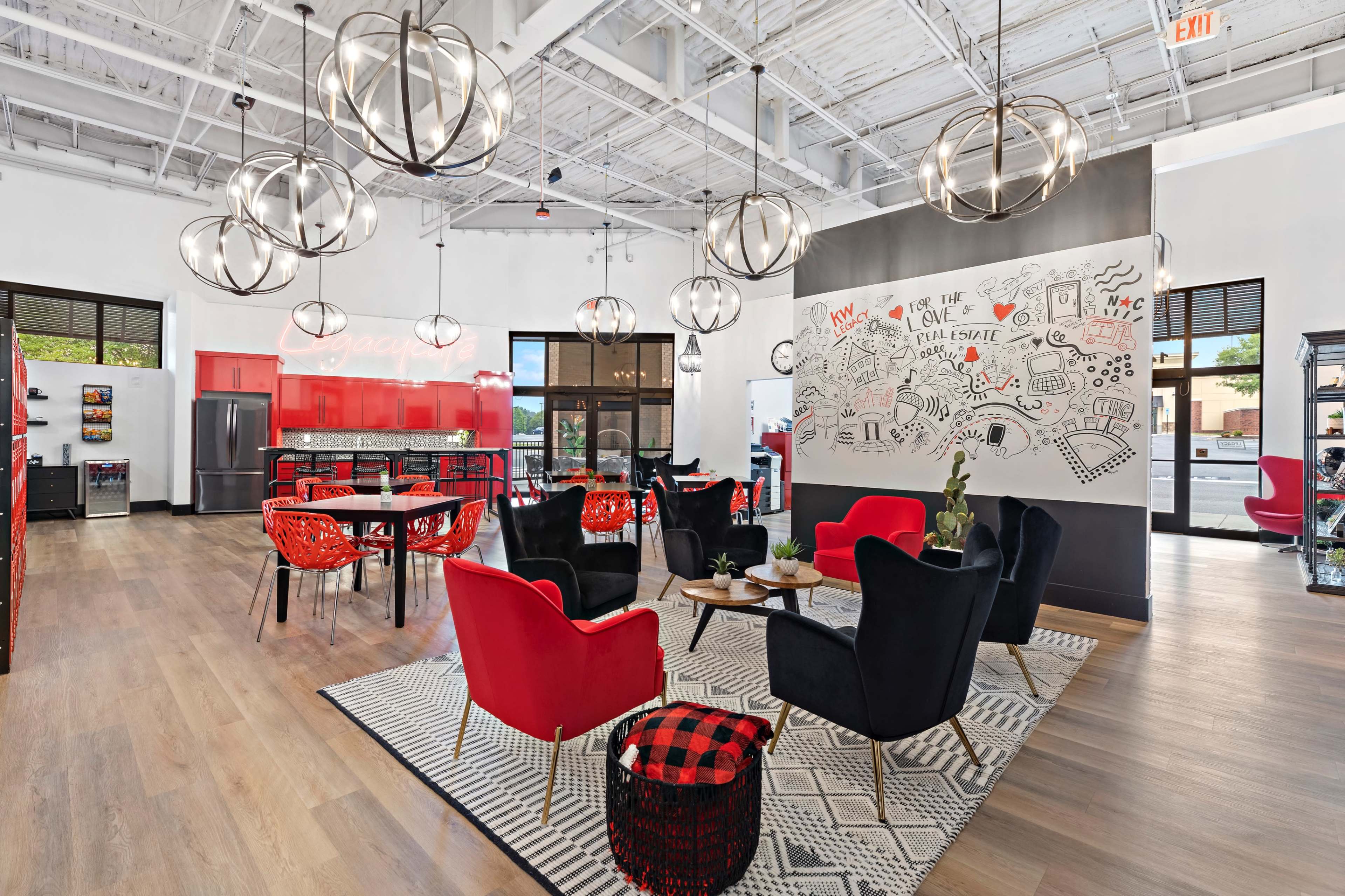 A modern office lounge features black and red furniture, pendant lights, and a large mural on the wall.