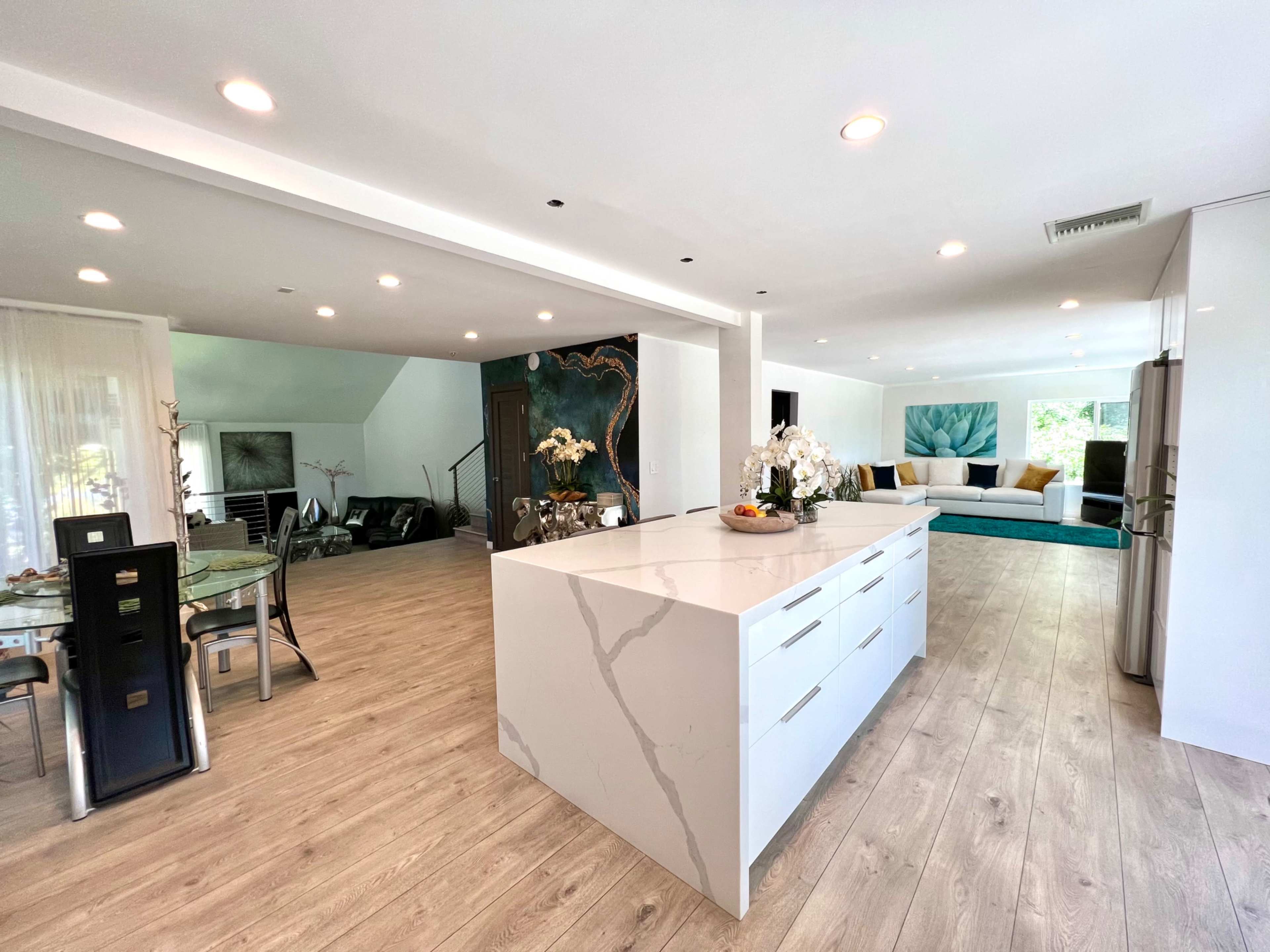 A modern open-concept living space features a sleek kitchen island, an adjacent dining area, and a cozy seating area with large windows.