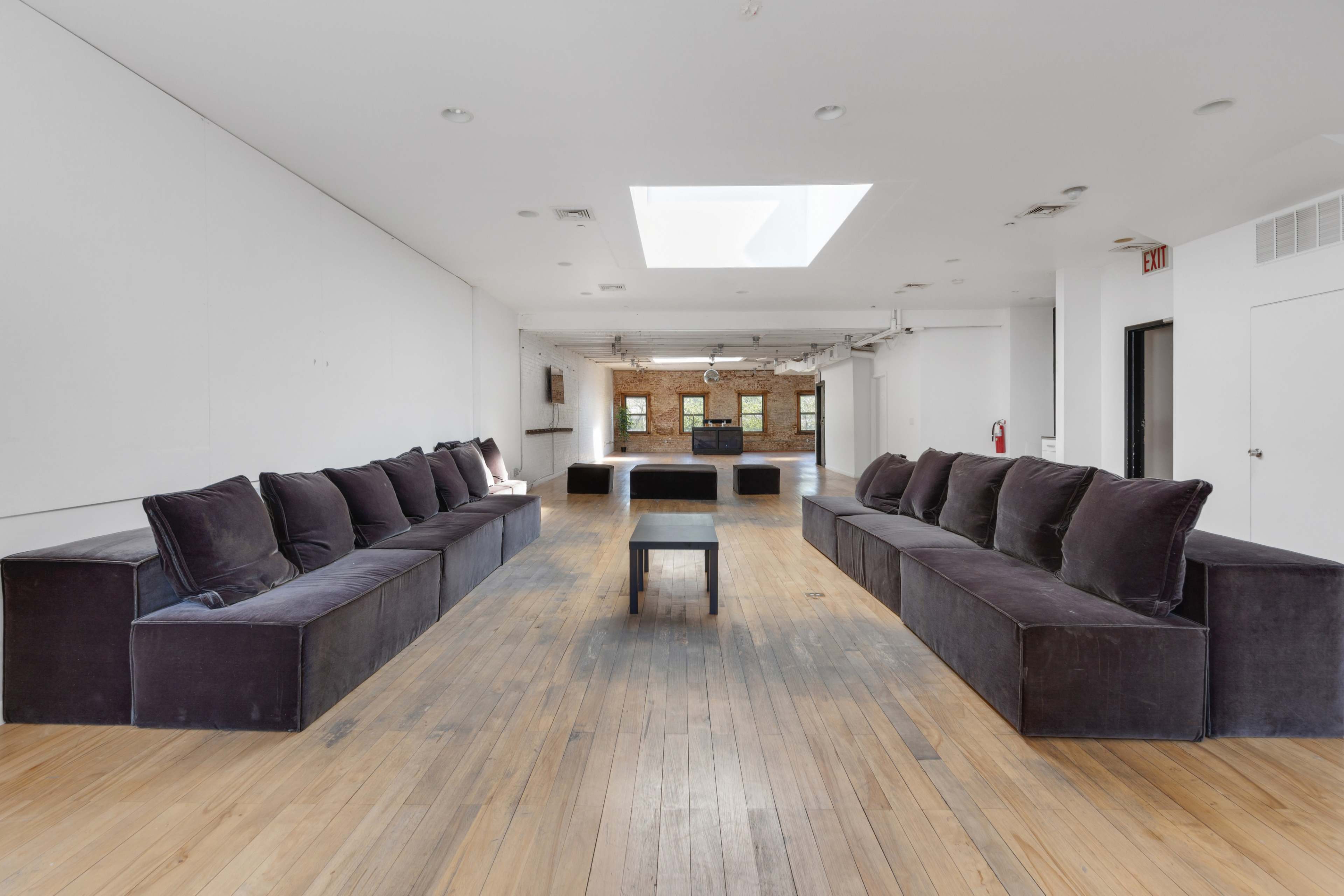 A spacious, minimalist room features two large sectional sofas facing each other, with a small table in the center and a skylight above.