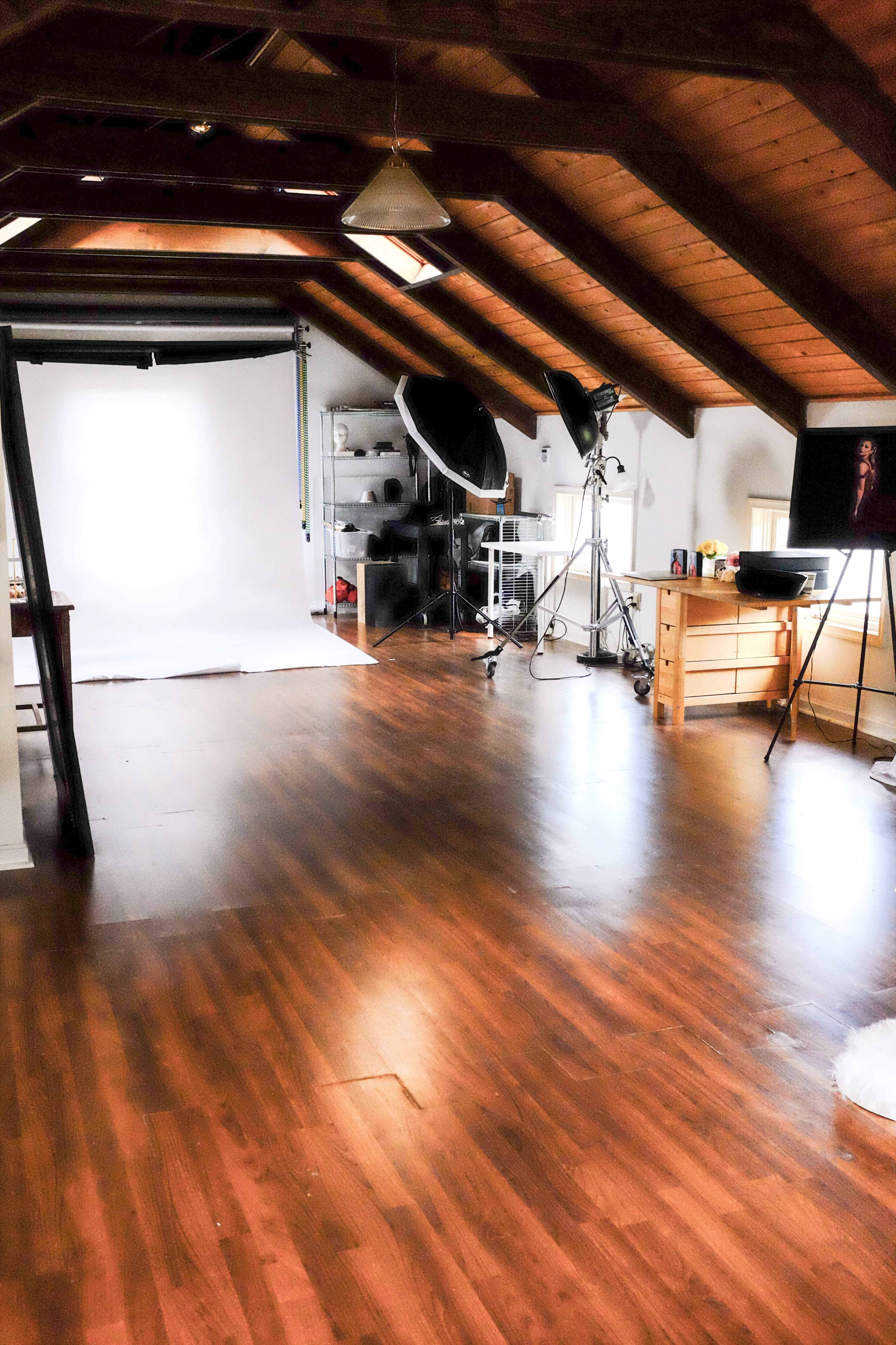 A spacious studio with wooden beams, a polished floor, and various photography equipment set up against a backdrop.