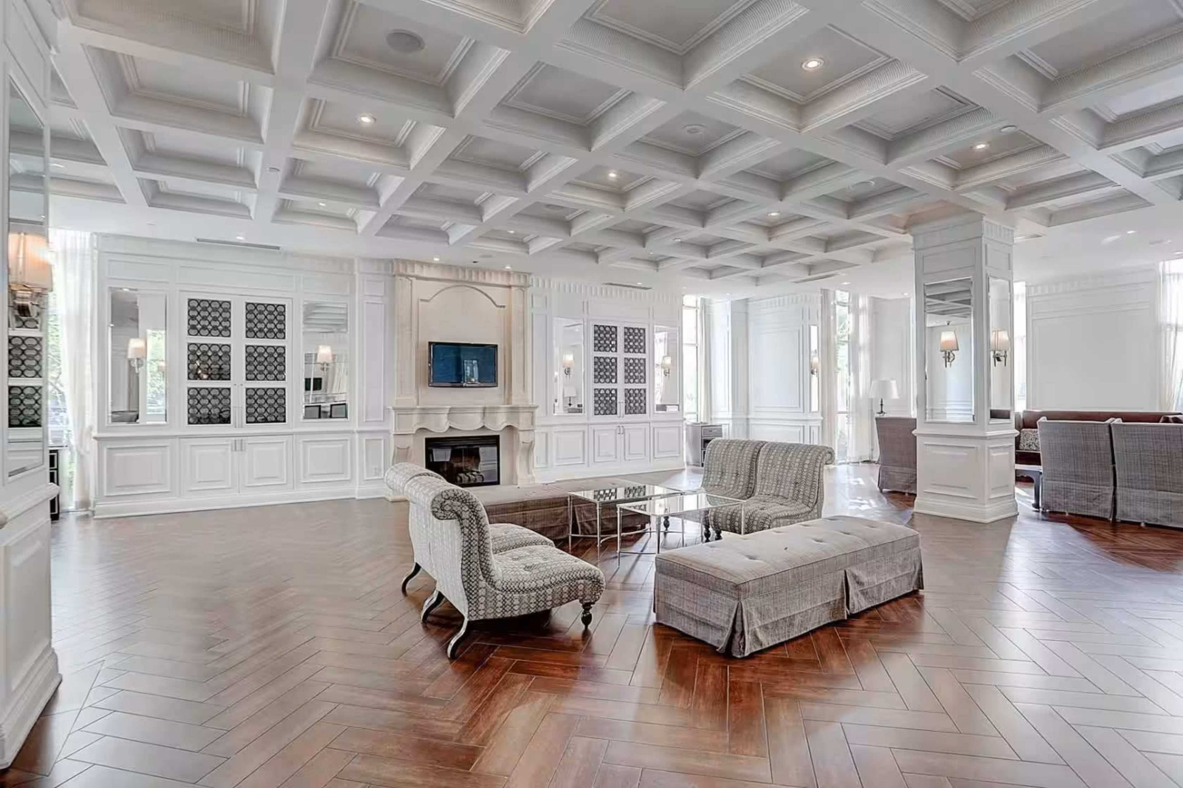 The room features a spacious layout with a coffered ceiling, hardwood flooring, and comfortable seating arrangements around a central coffee table.