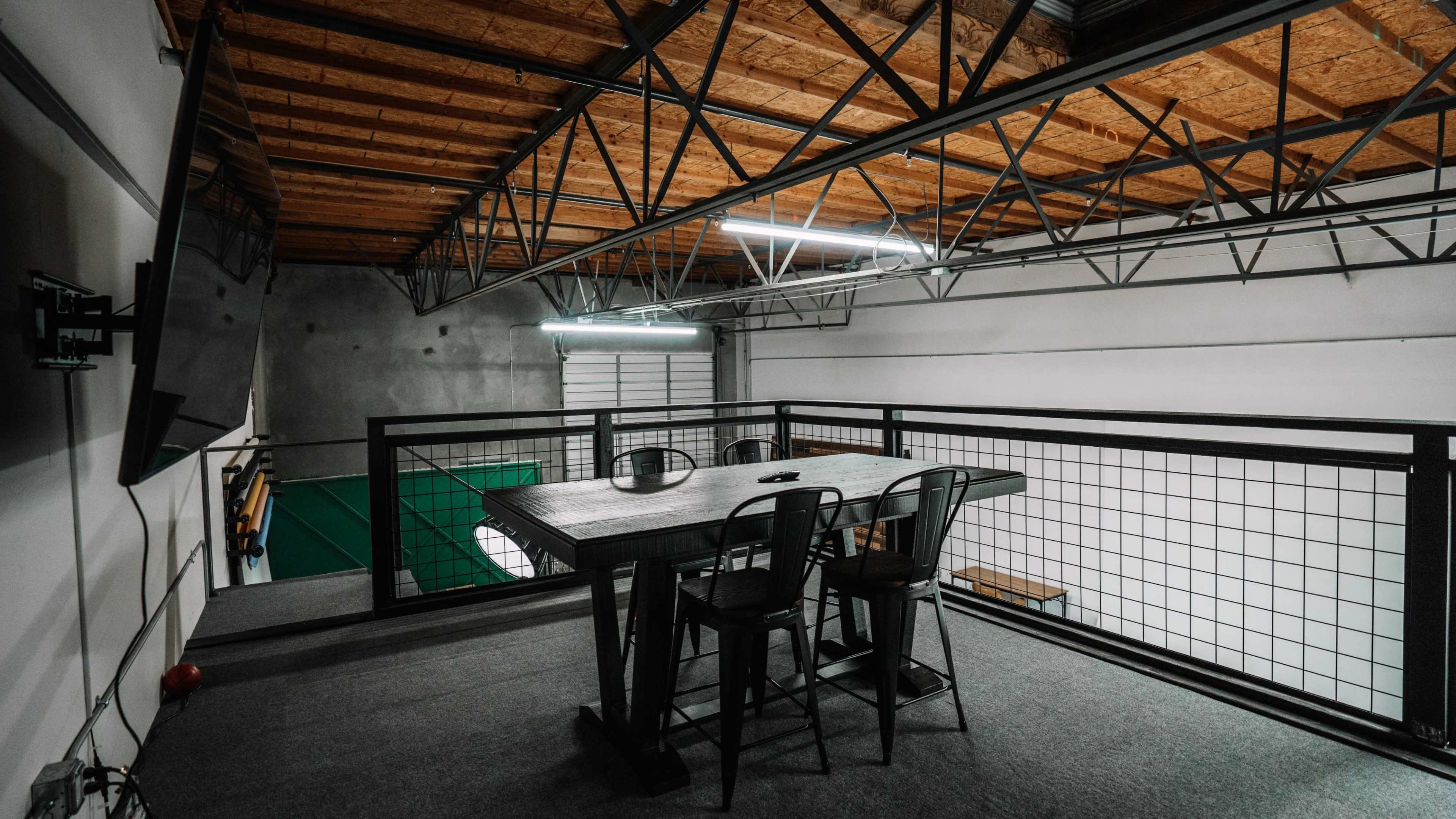 A spacious loft area features a table with chairs, overlooking a large open room fitted with a green surface.
