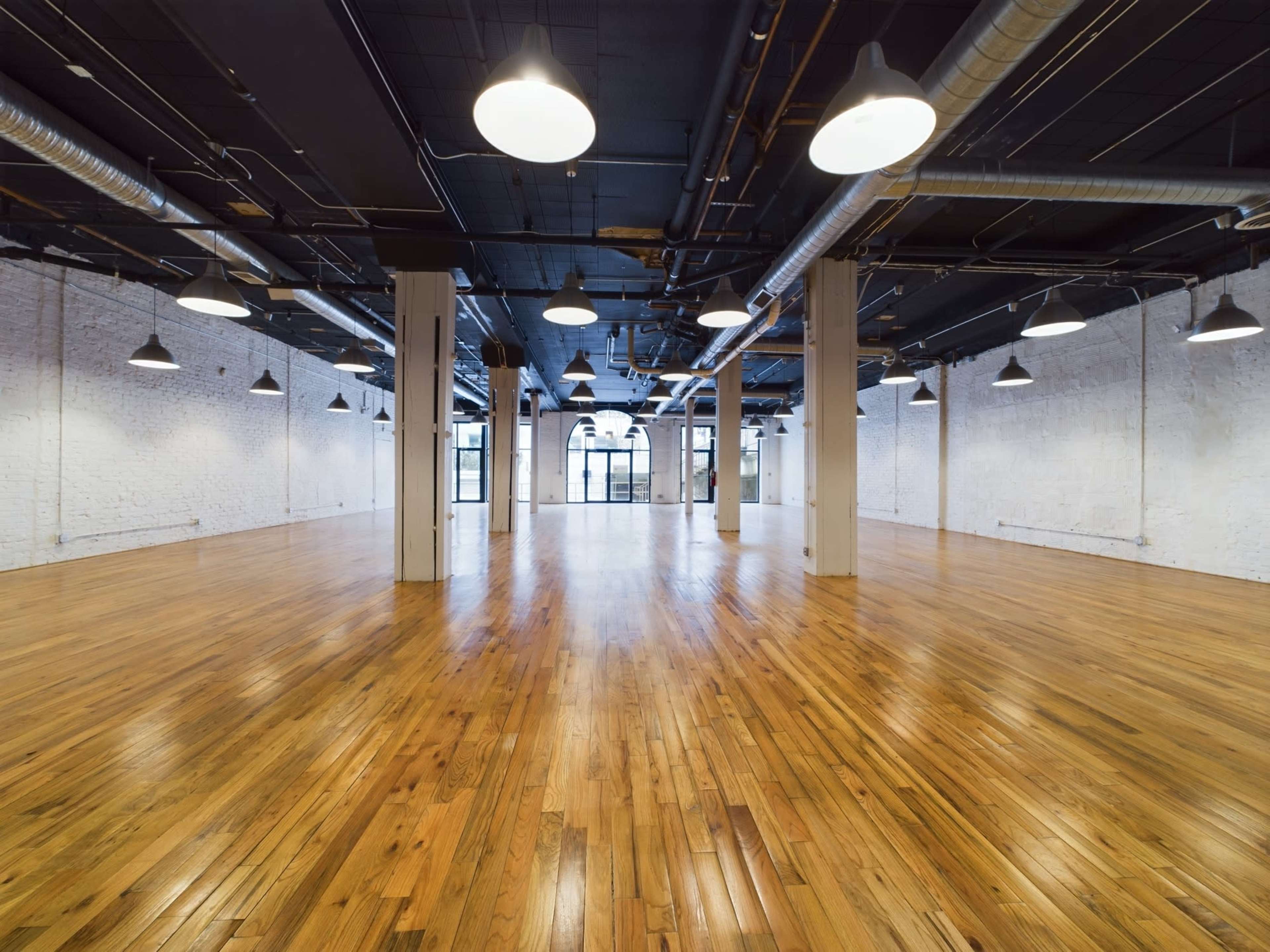 An empty, spacious room with polished wooden floors and industrial-style lighting.