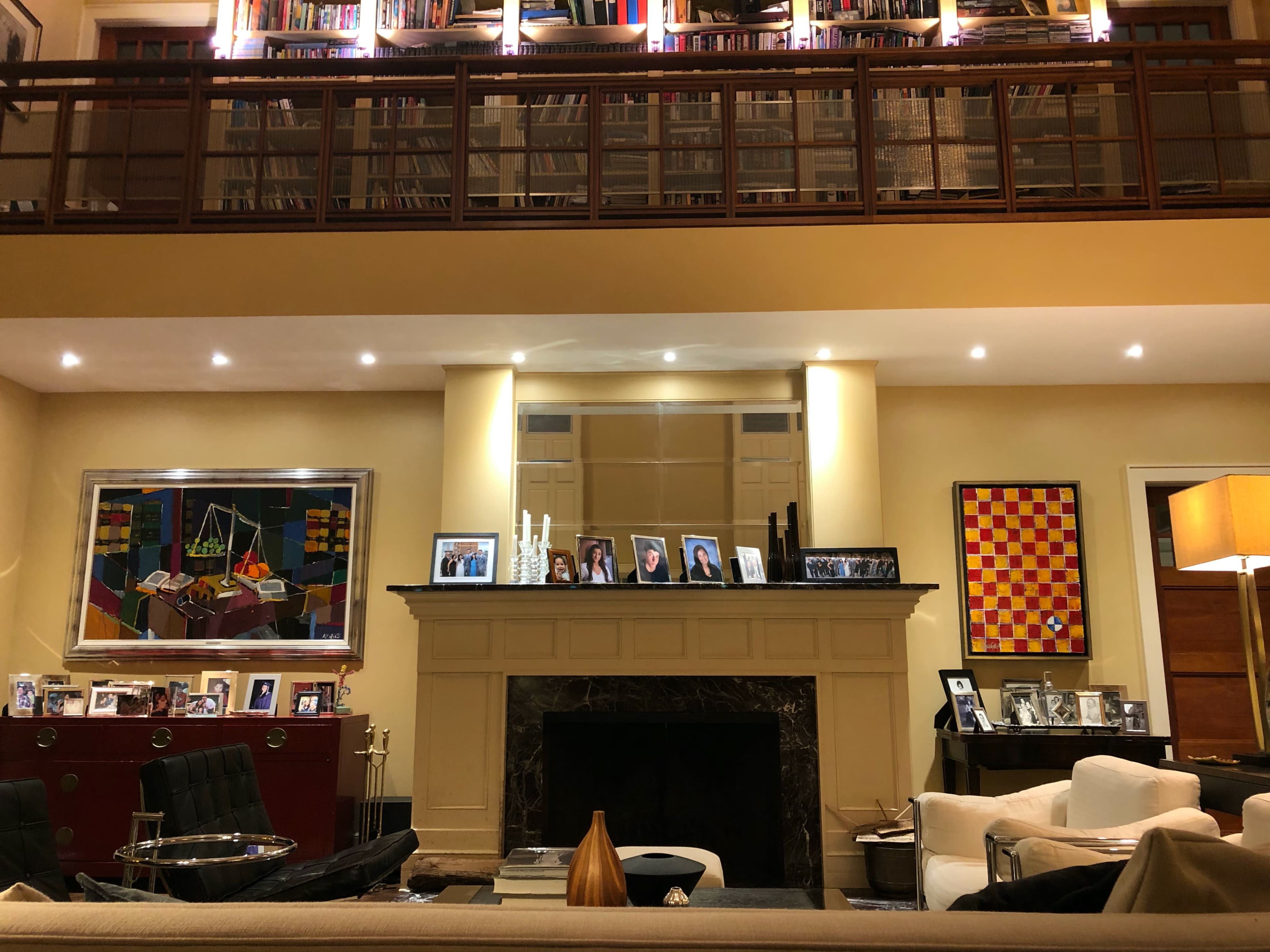 A living room with a fireplace, bookshelves above, a collection of framed photos on the mantel, and artwork on the walls.