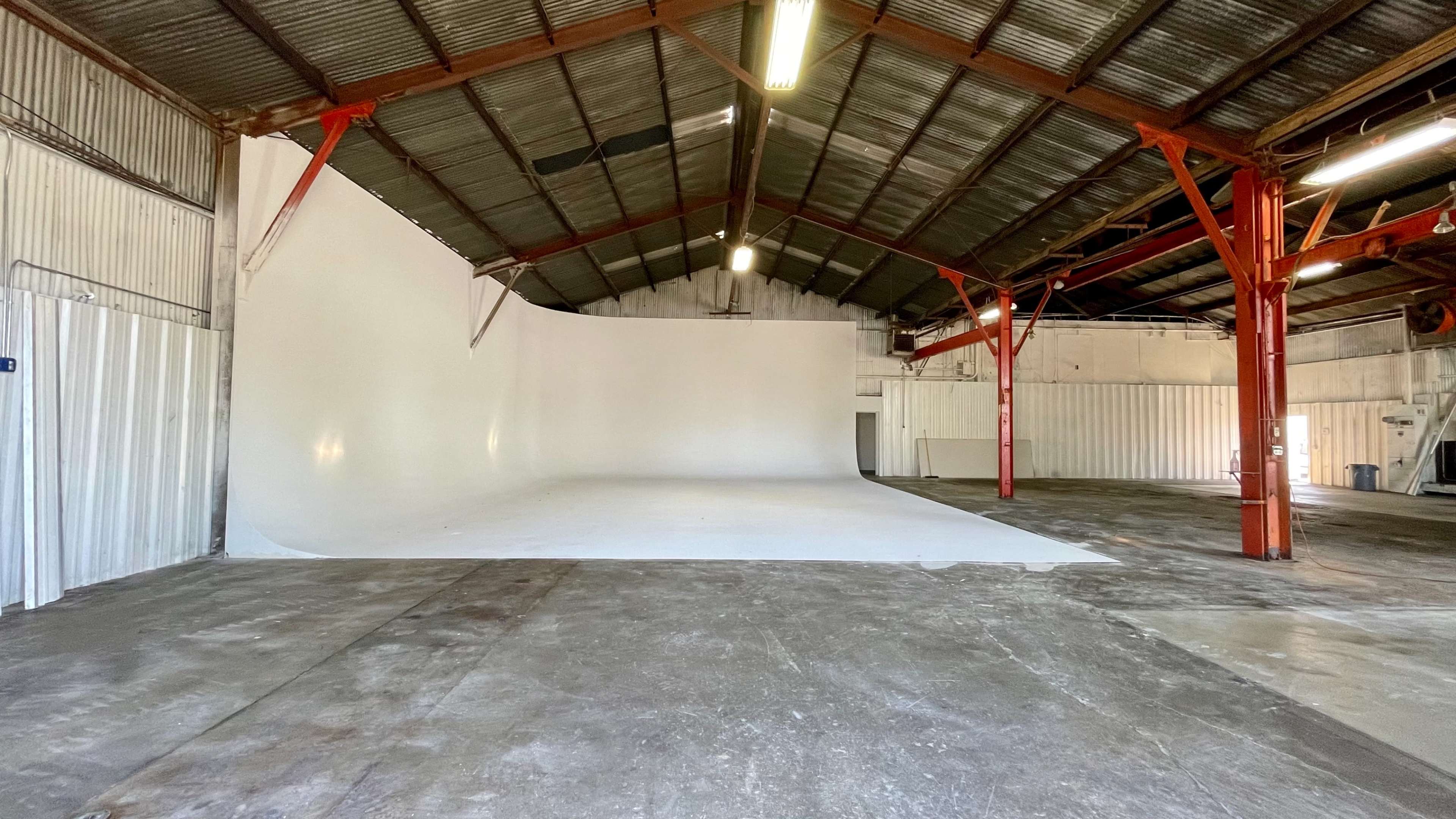 A spacious industrial warehouse with a large white curved backdrop and exposed metal beams.