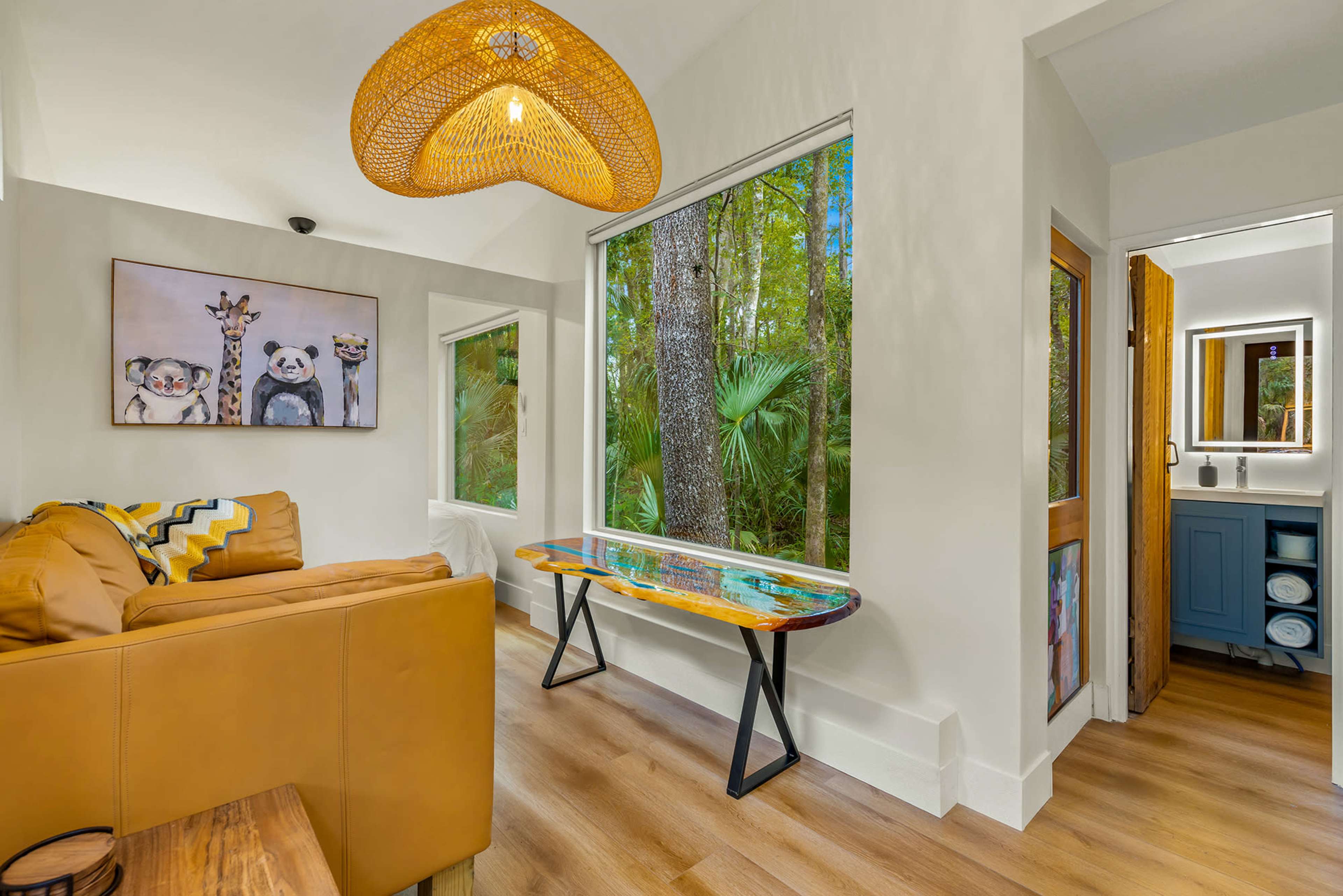 A cozy living space features a yellow sofa, a decorative lamp, and a table with a view of lush greenery outside.