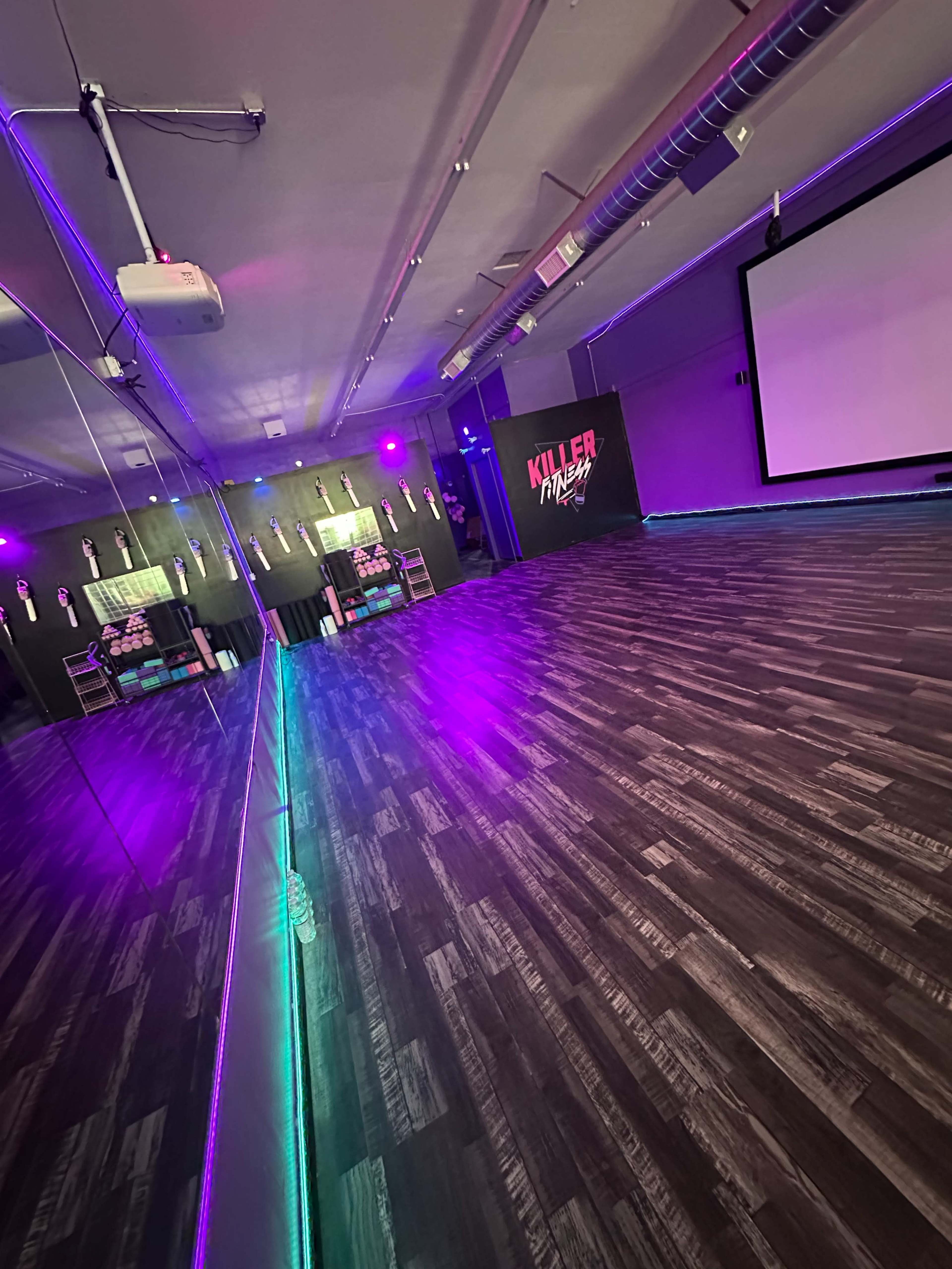 A dance studio features a mirrored wall, a projector screen, and purple ambient lighting.