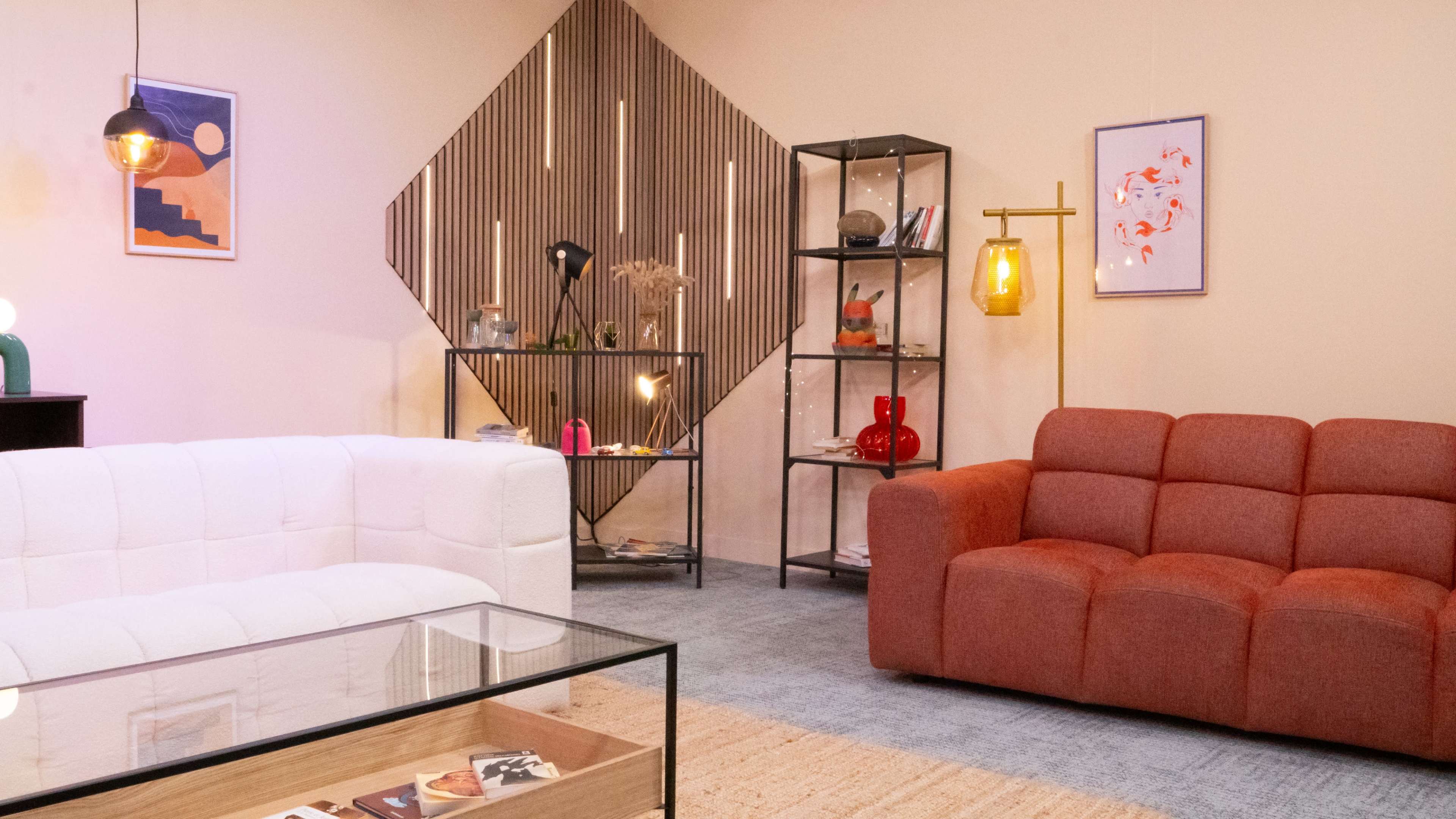 The image depicts a modern living room with a white sofa, a red sofa, a glass coffee table, artwork on the walls, and a decorative shelving unit.