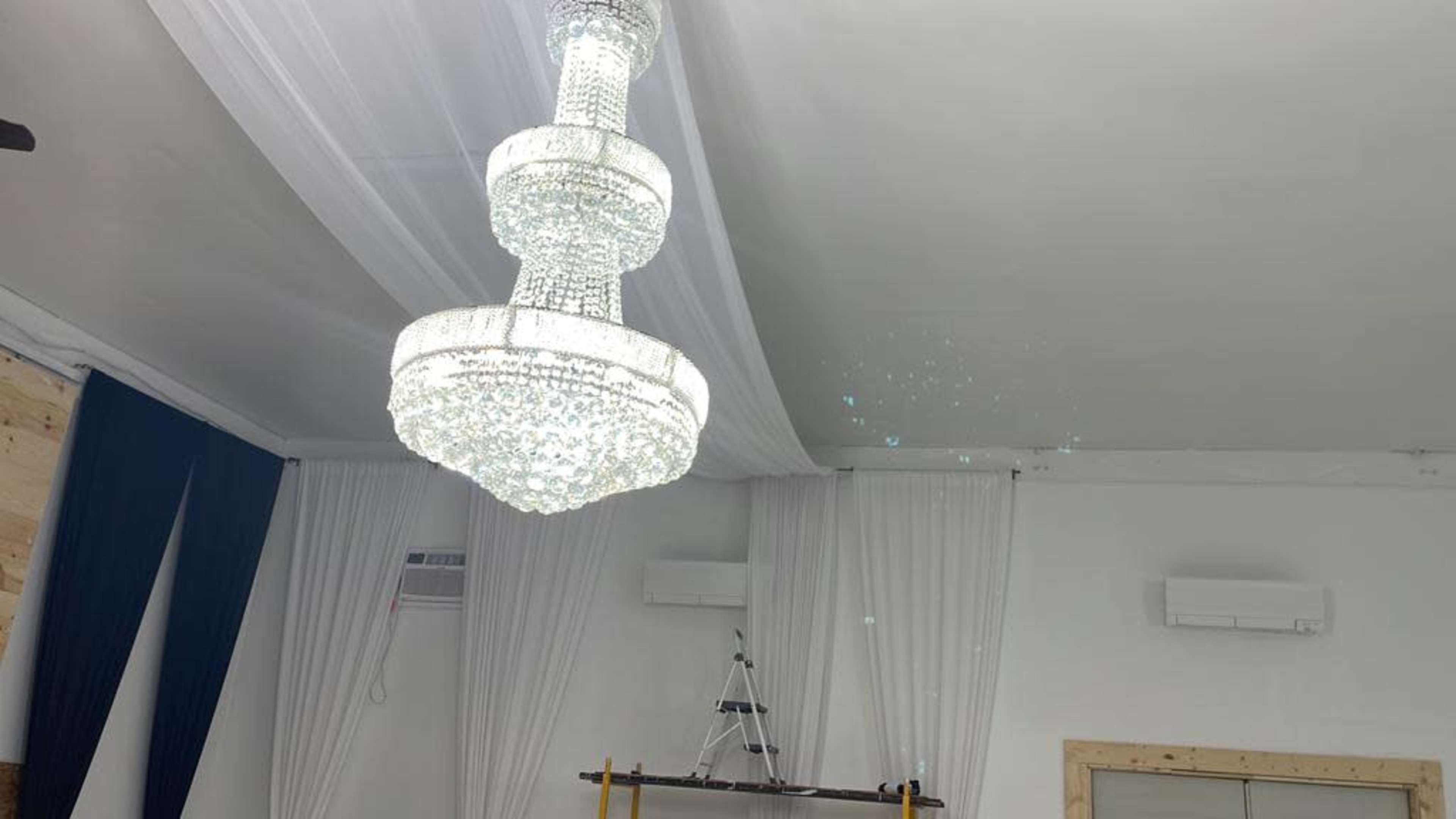 The image shows a modern chandelier hanging from a white ceiling, with sheer drapes on the walls.