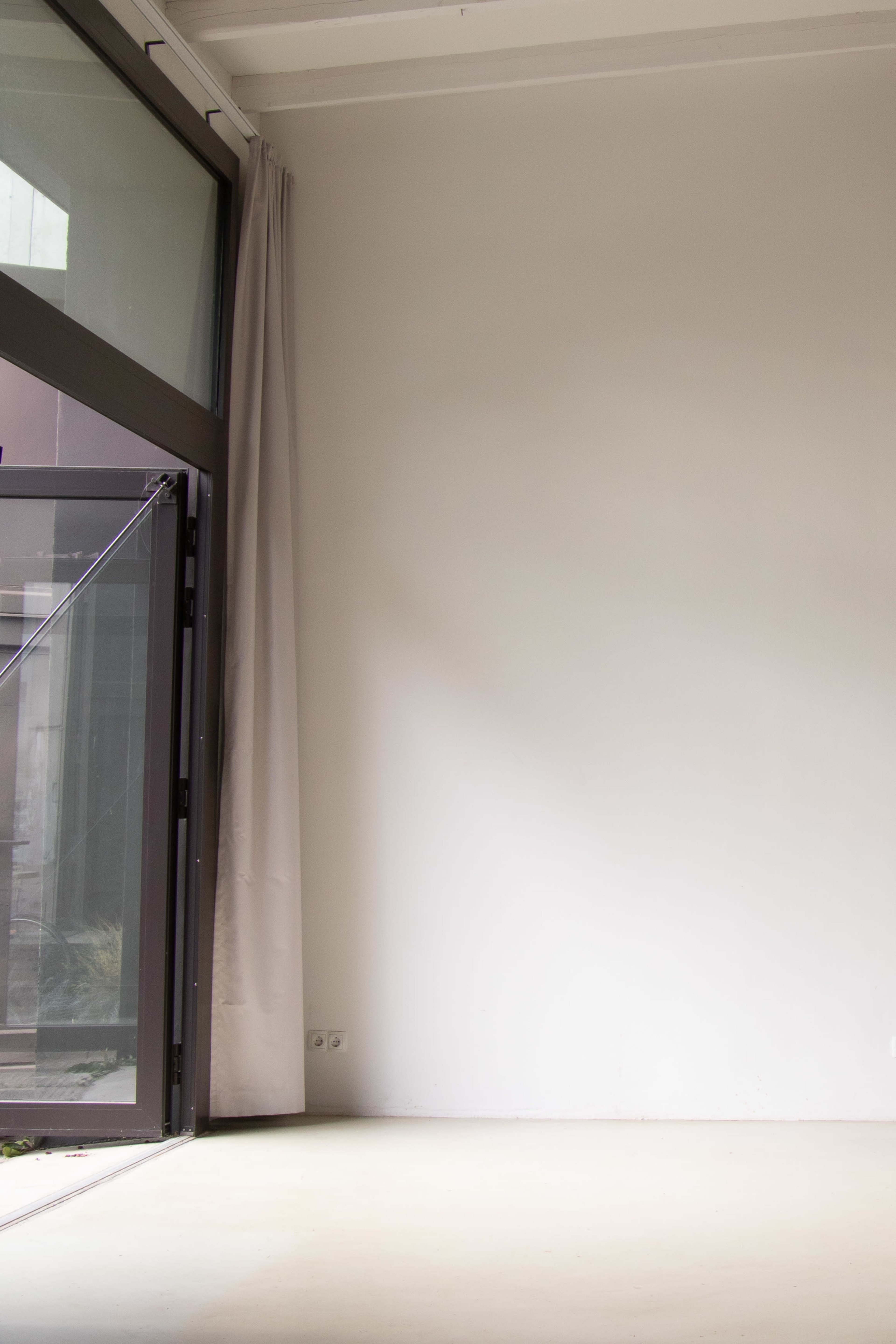 The image shows an empty room with a large window partially open, revealing a plain wall and a light curtain.