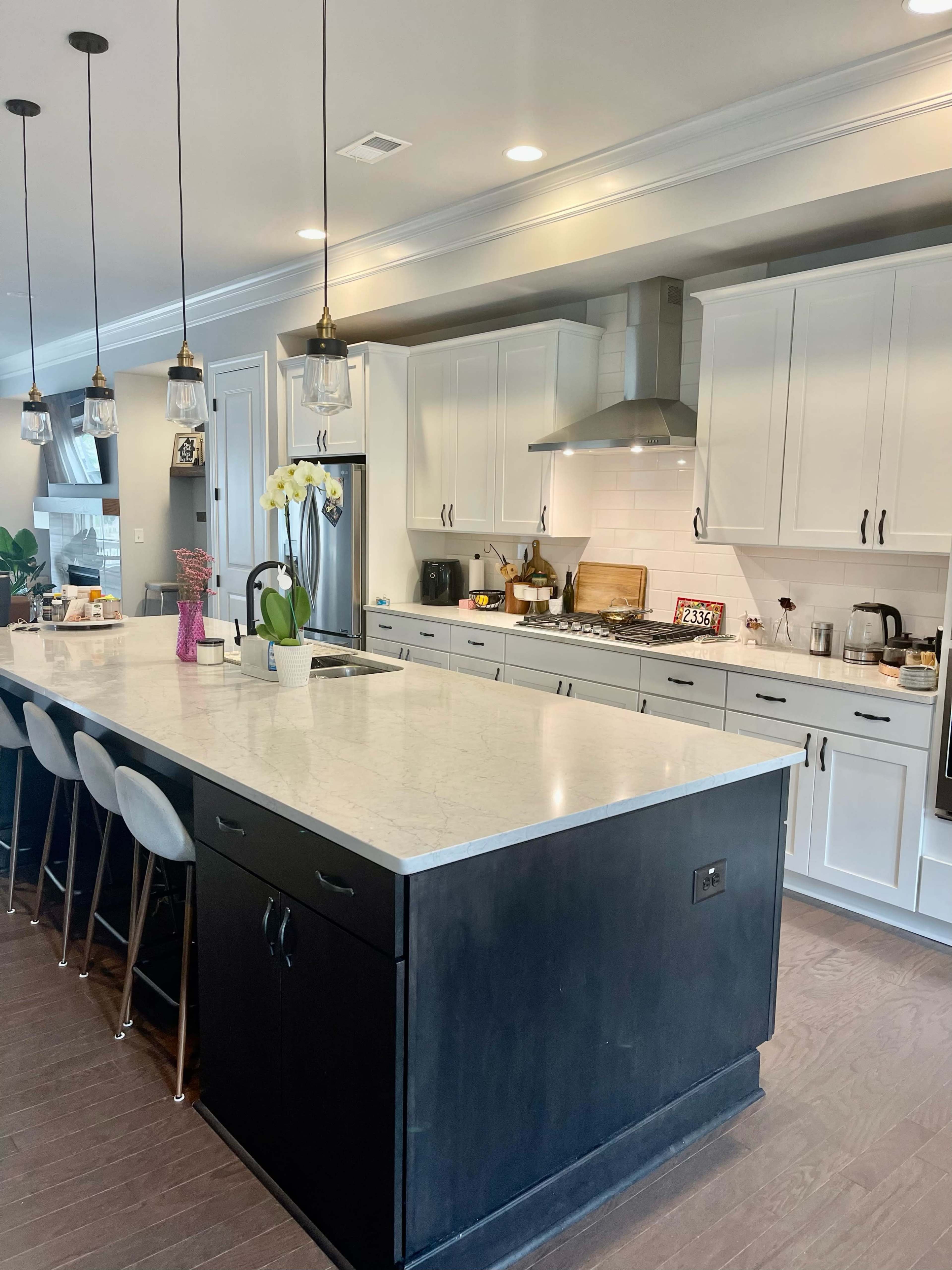 A modern kitchen features a large island with bar seating, white cabinets, and stainless steel appliances.