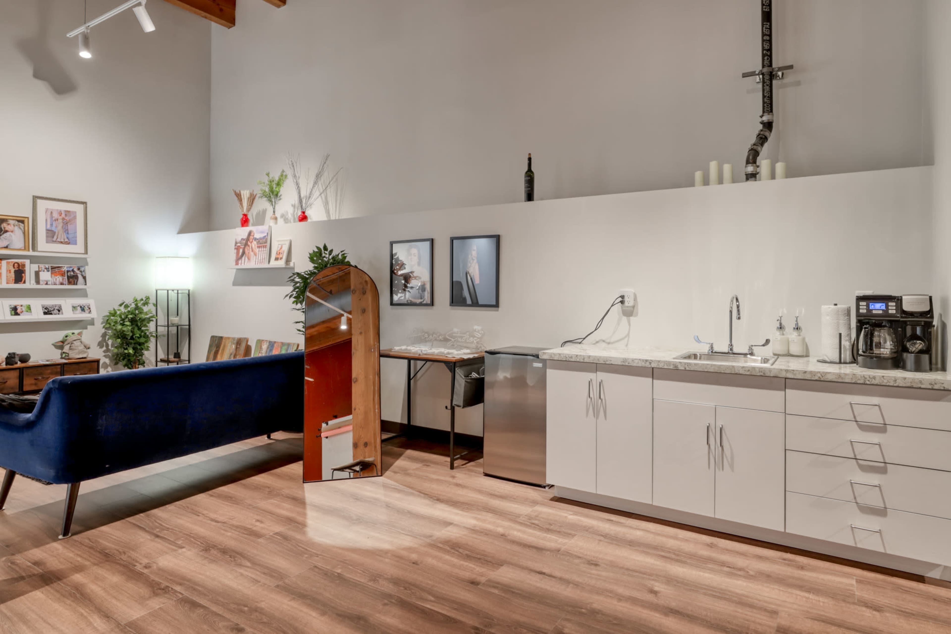 The image shows a modern kitchen area with a blue sofa, a mirrored arch, a countertop with appliances, and framed artwork on the wall.