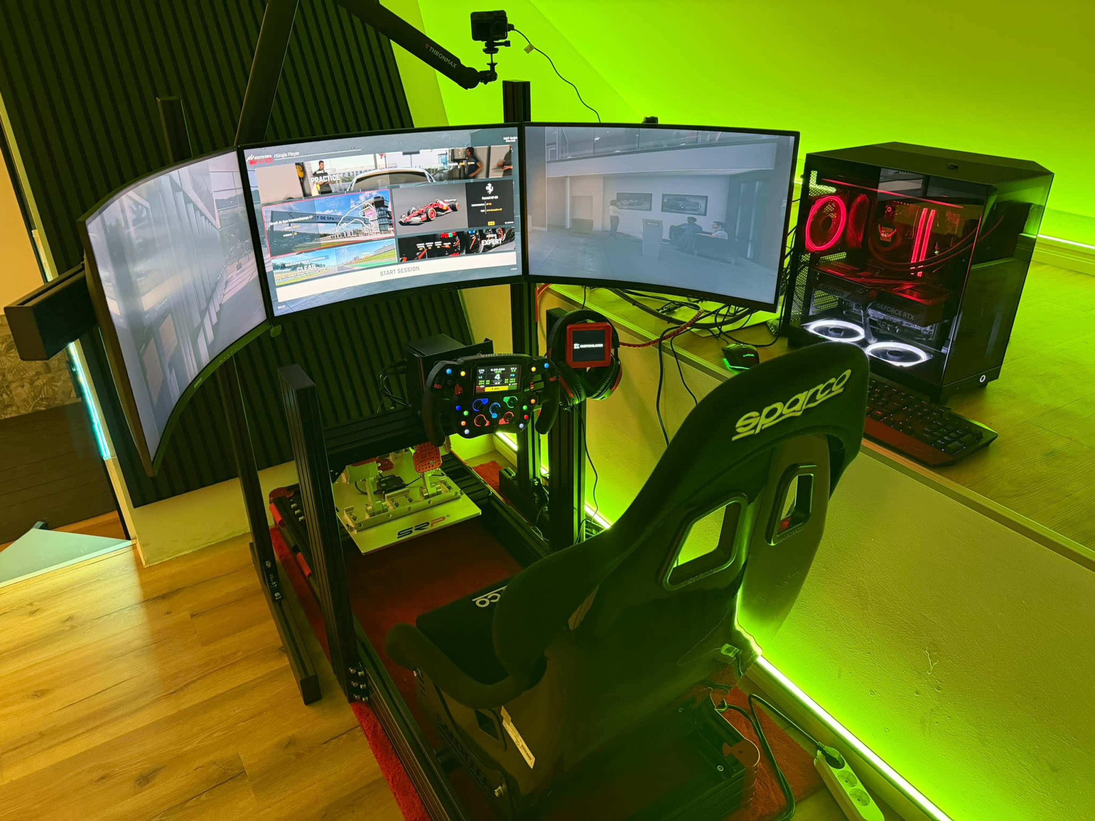 The image shows a racing simulator setup featuring three curved monitors, a racing wheel, and a gaming chair, all illuminated by green ambient lighting.