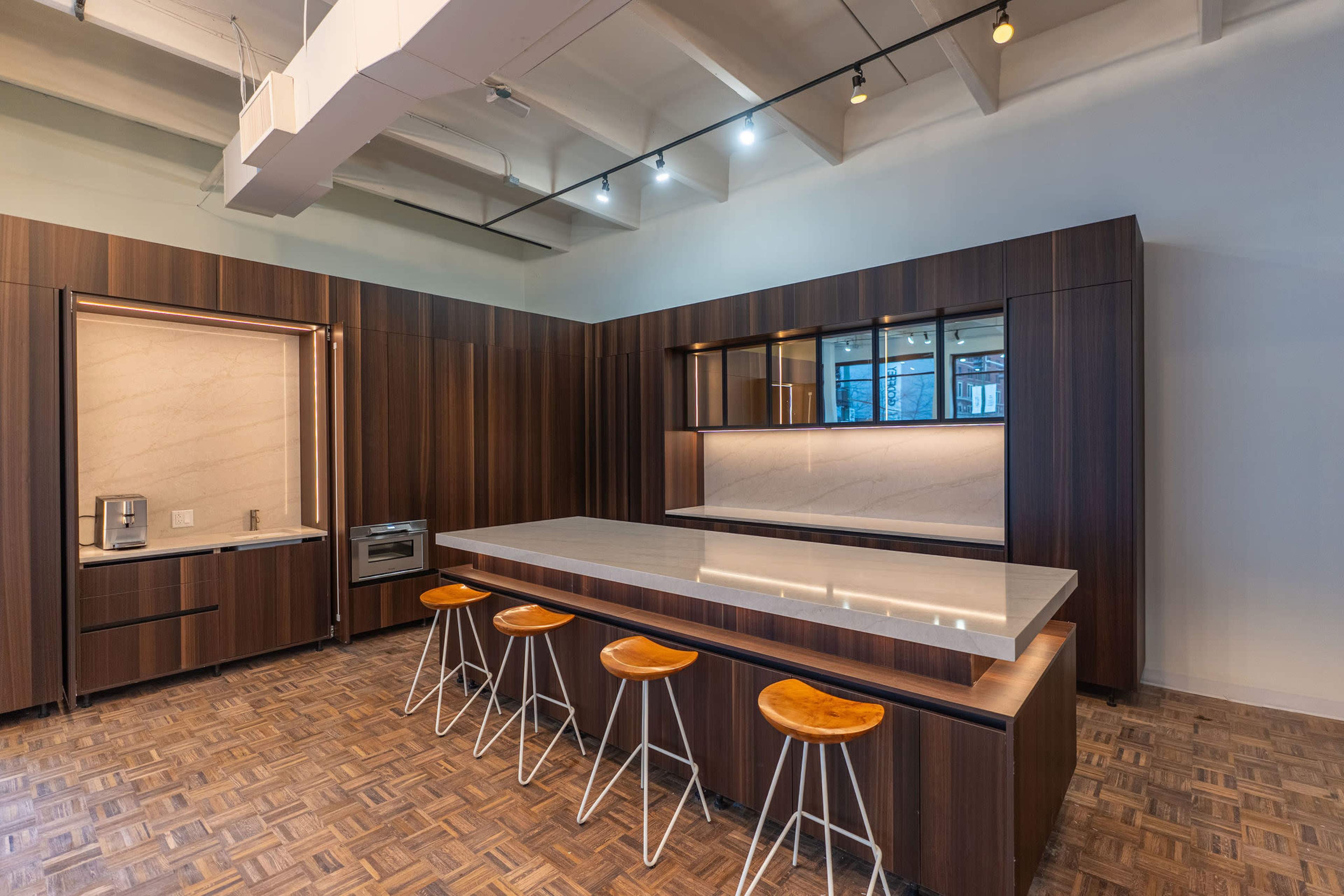 The image shows a modern kitchen featuring dark wood cabinetry, a marble countertop island with four wooden bar stools, and stainless steel appliances.