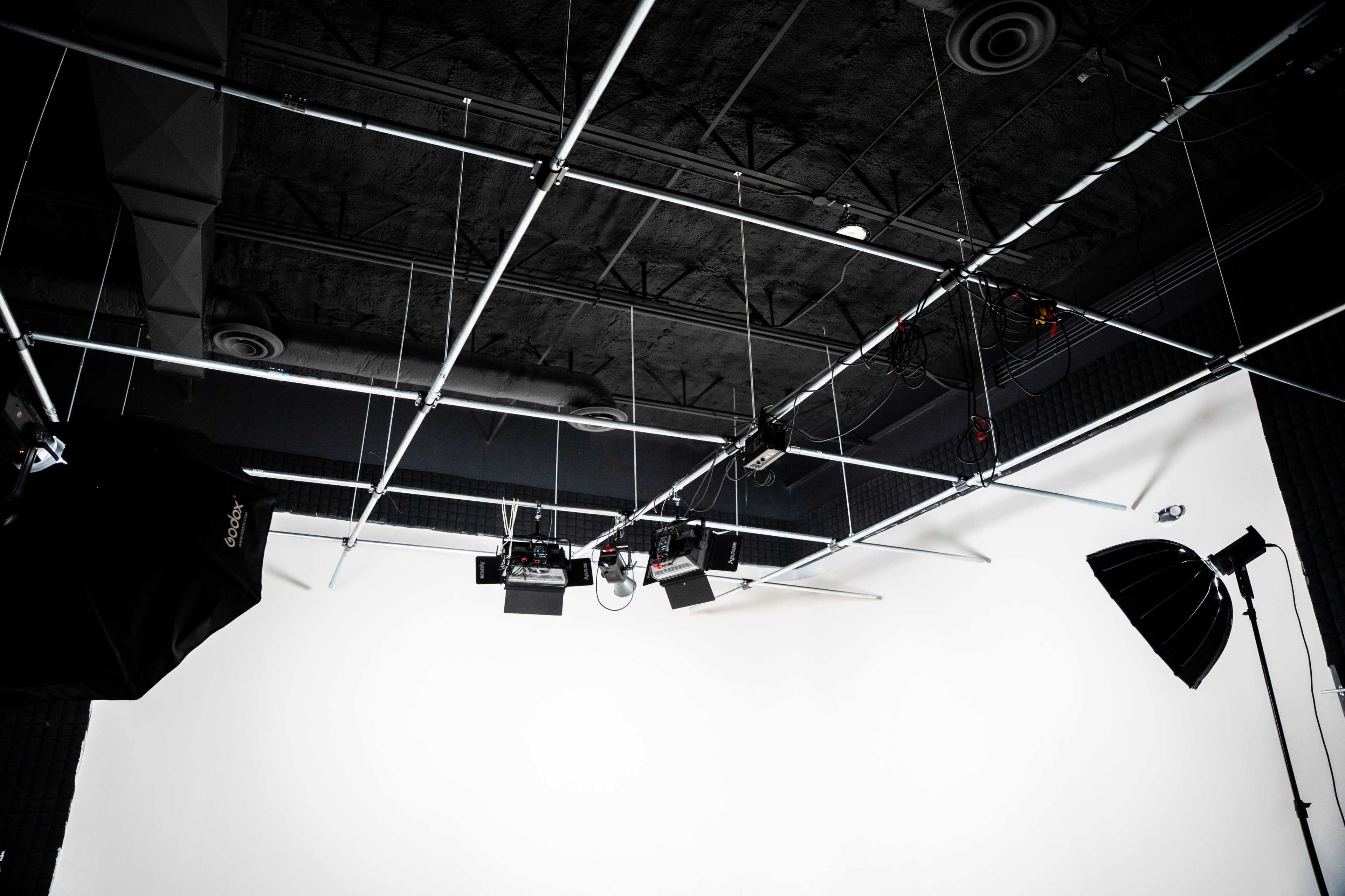 The image shows a photography studio setup with overhead lighting and a blank backdrop.