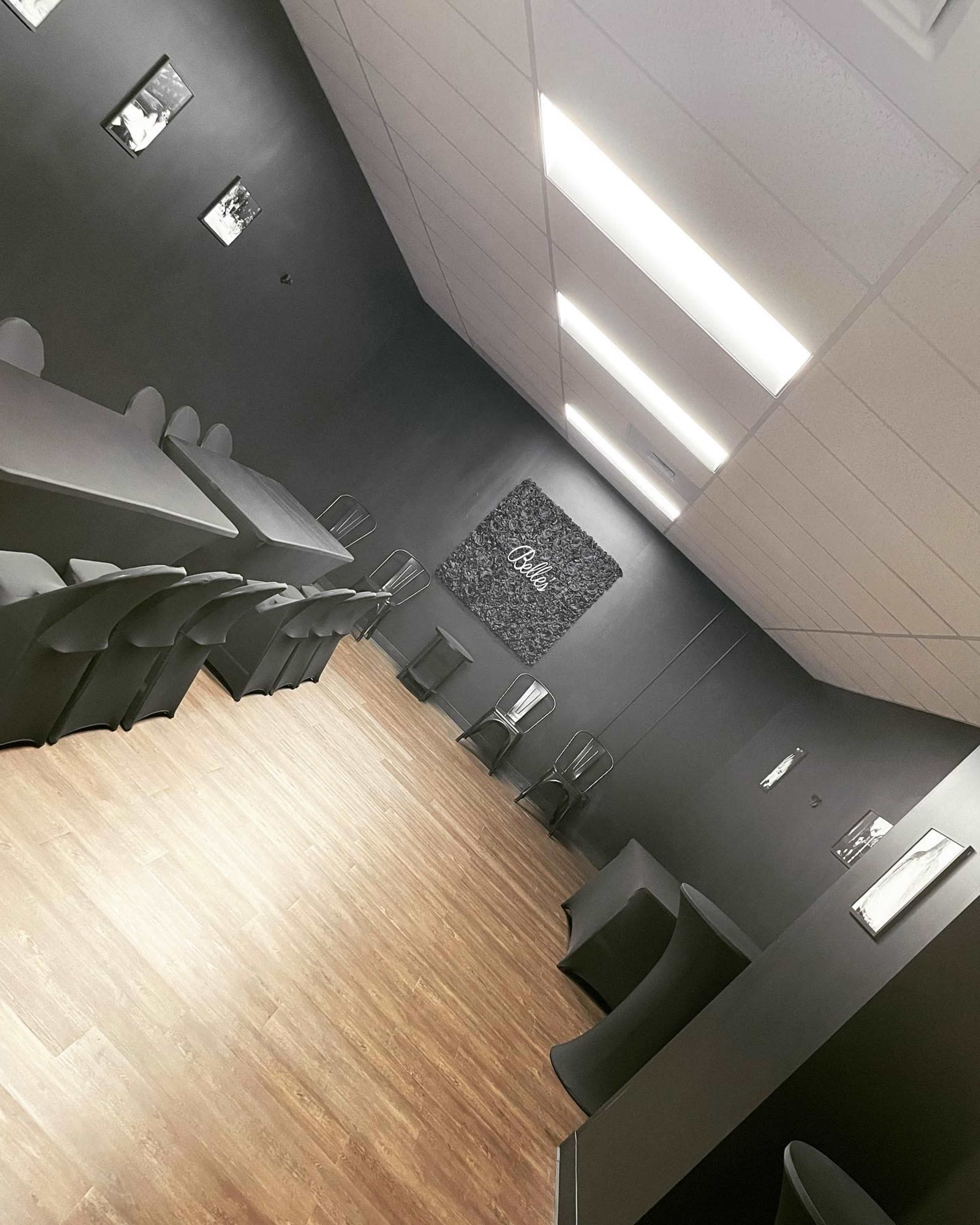 A spacious, modern room with gray walls, wooden flooring, and multiple seating arrangements, including tables and chairs along the sides.