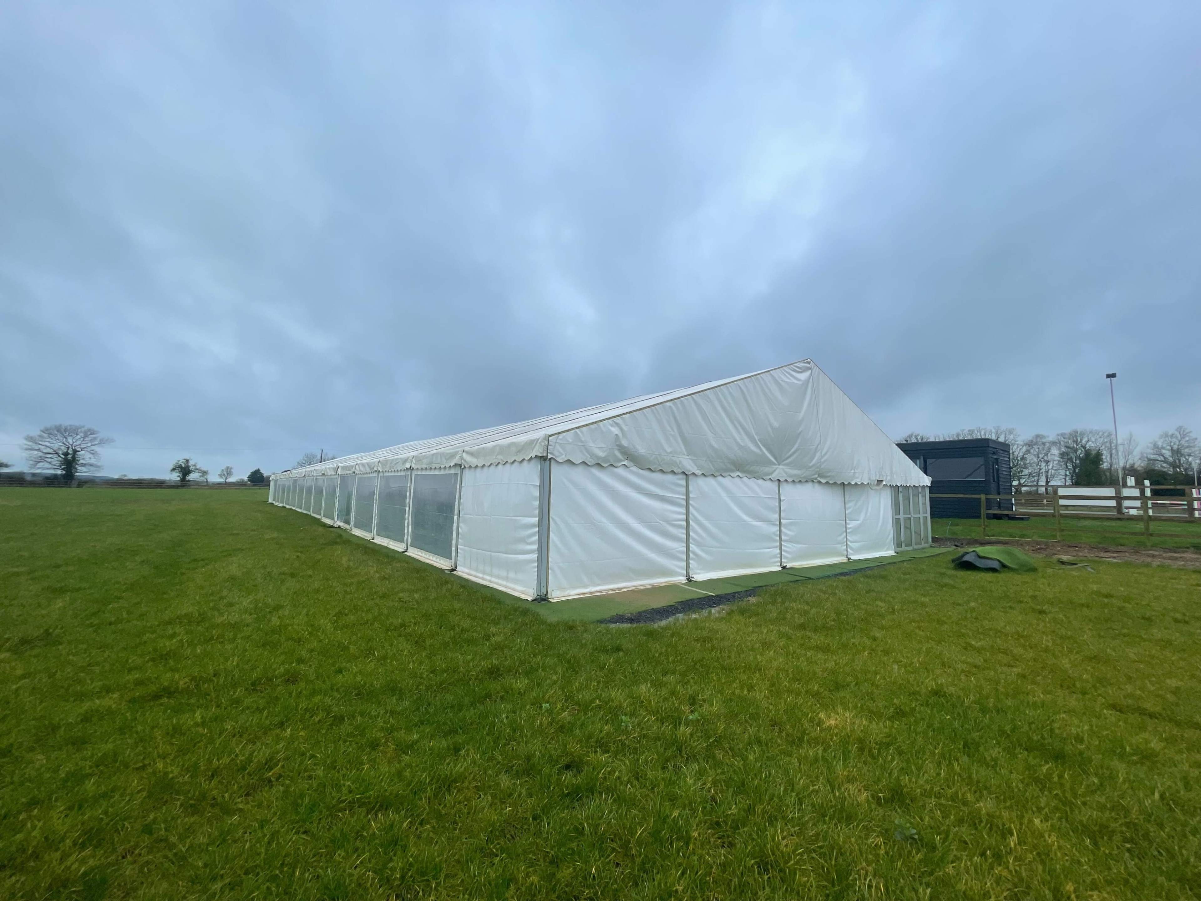 A large white marquee tent is set up on a grassy field under a cloudy sky.